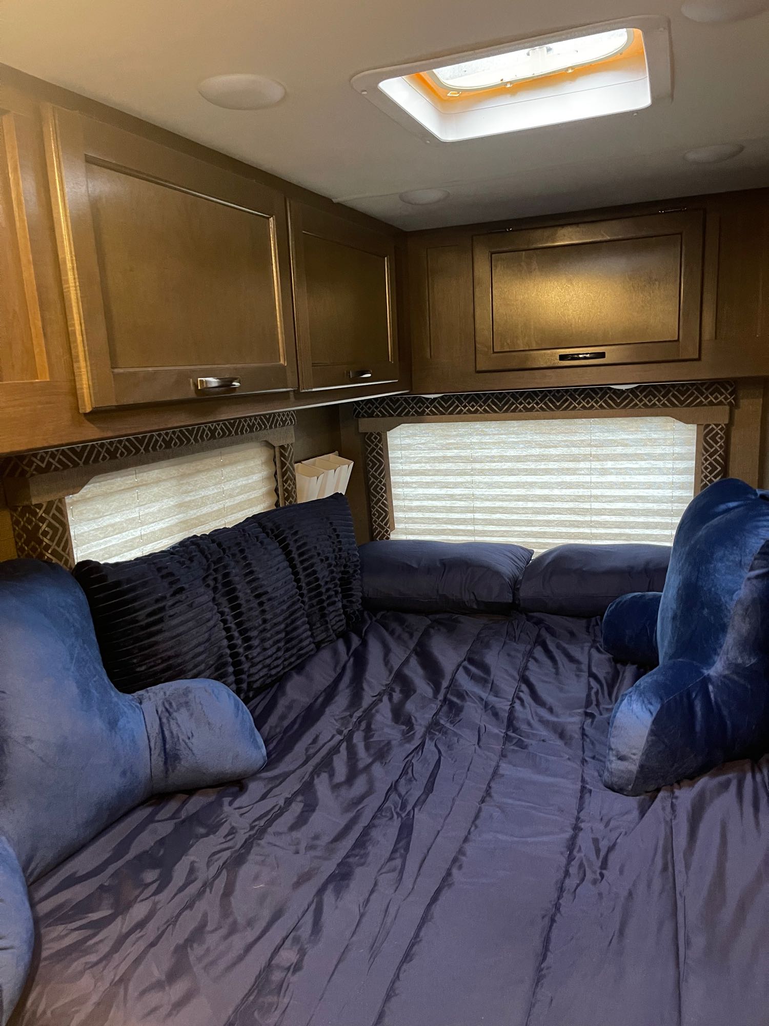 **RV rental** bedroom: a comfy bed with blue bedding, overhead cabinets, a window, and a bright skylight. Ready for travel!. Thor Four Winds 2018