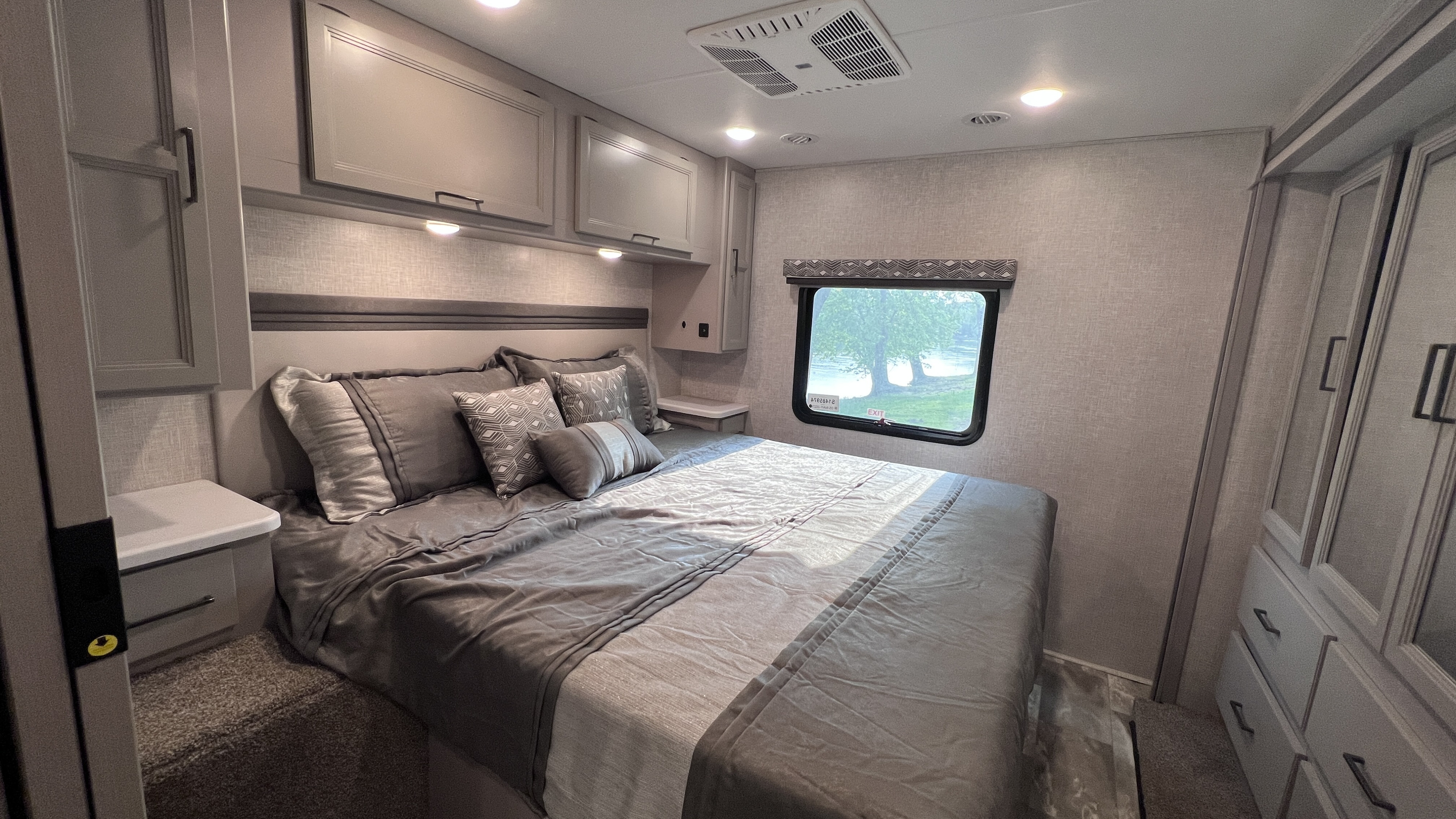 Modern RV rental bedroom with a comfortable bed, gray bedding, ample built-in storage, and a window showcasing a scenic view.. Thor Windsport 2023