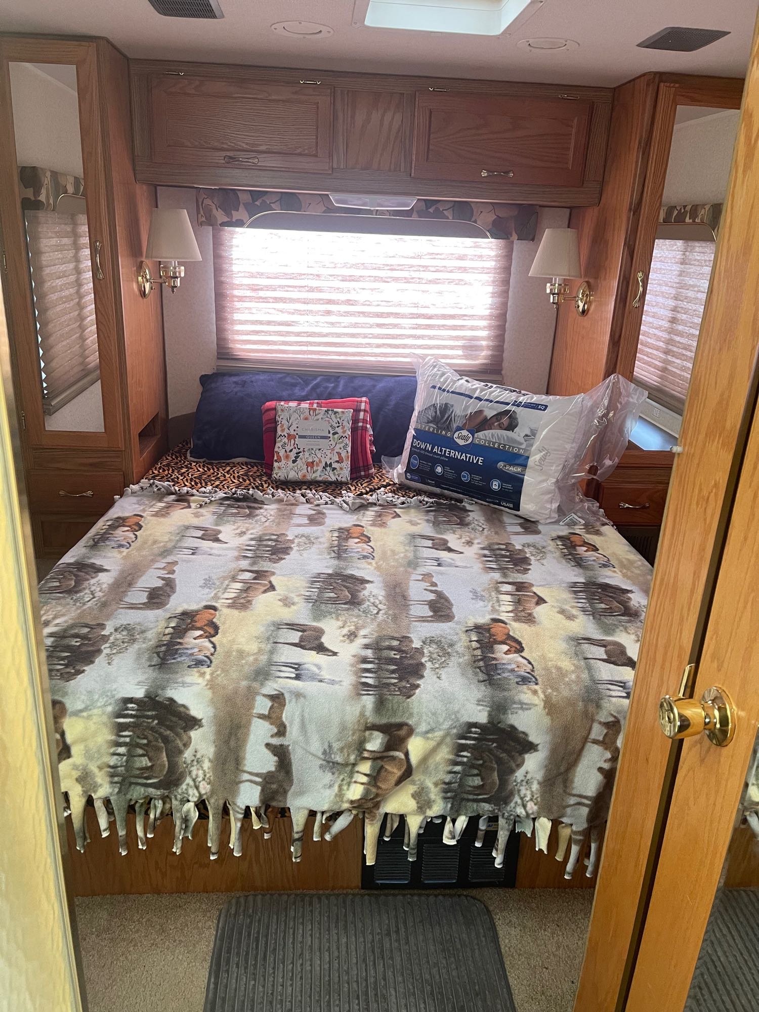 Cozy RV rental bedroom featuring a bed with a wildlife-patterned blanket, new pillow, and ample wooden storage.. Gulf Stream Conquest 2000