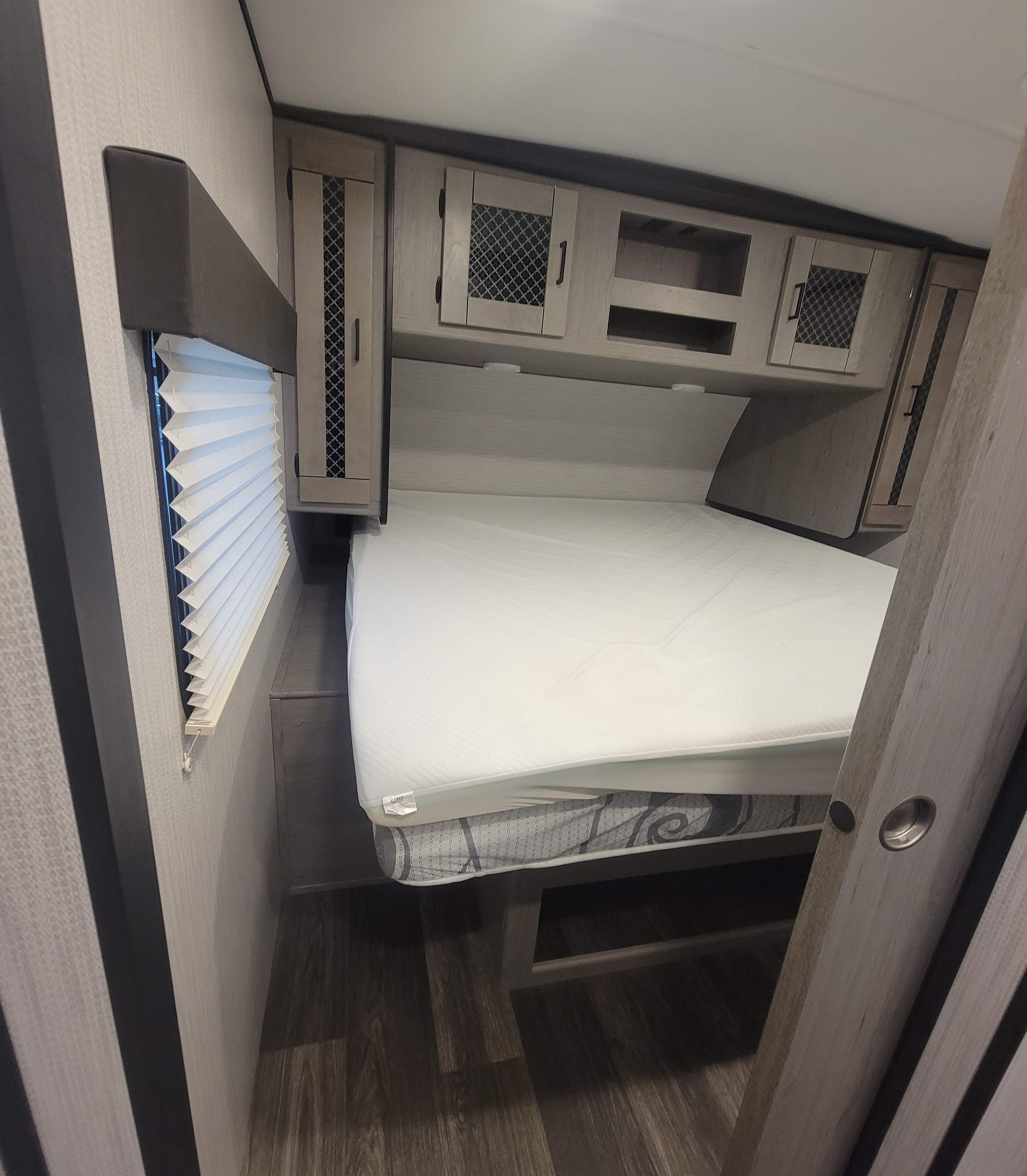 Compact RV rental bedroom featuring a bed, overhead cabinets, and a window with blinds. Ideal for comfortable travel.. Heartland RVs Mallard 2021
