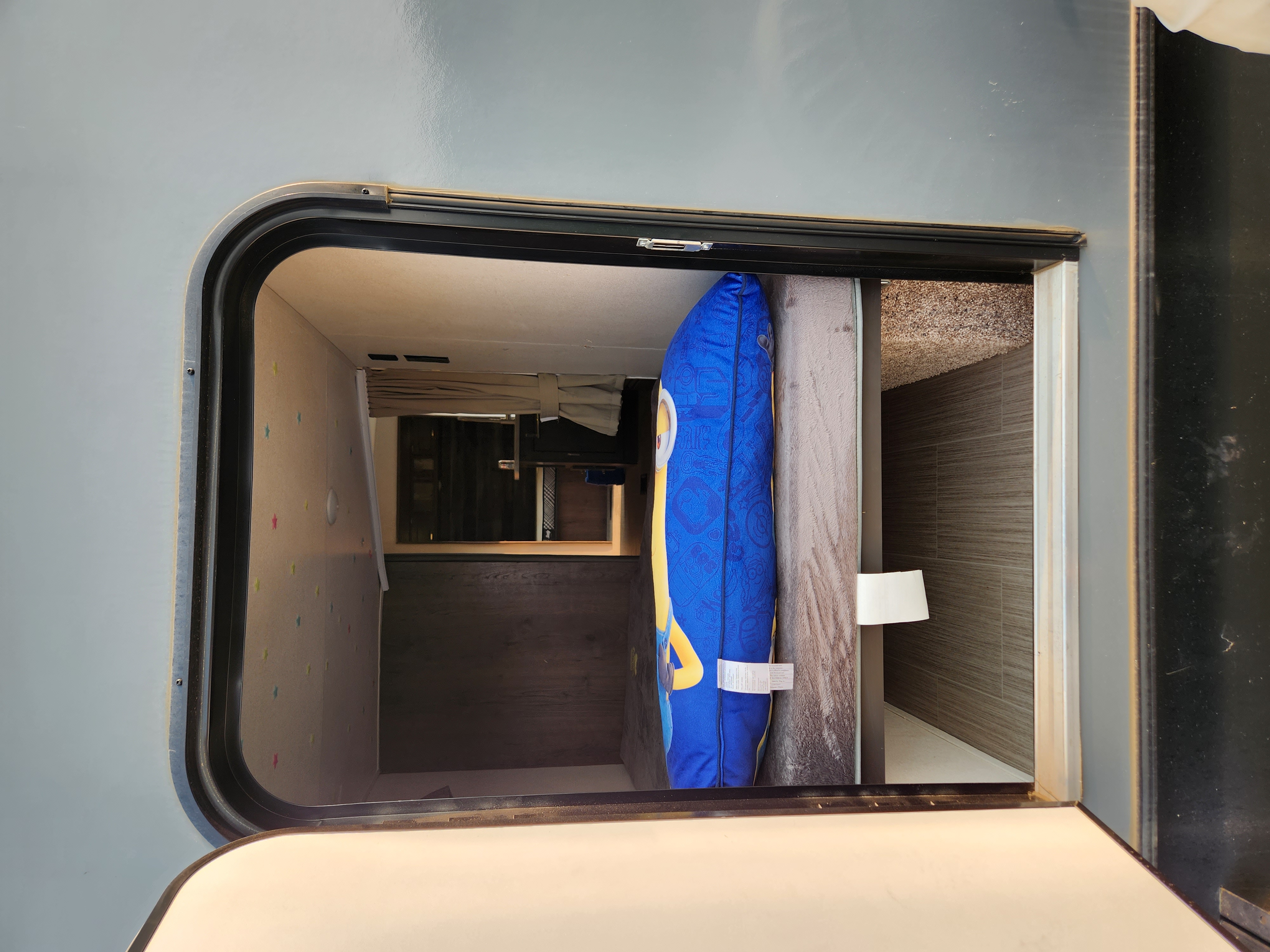 A view inside an RV rental's accessible storage compartment or bunk, featuring a blue Minion pillow.. Keystone RV Passport GT 2021