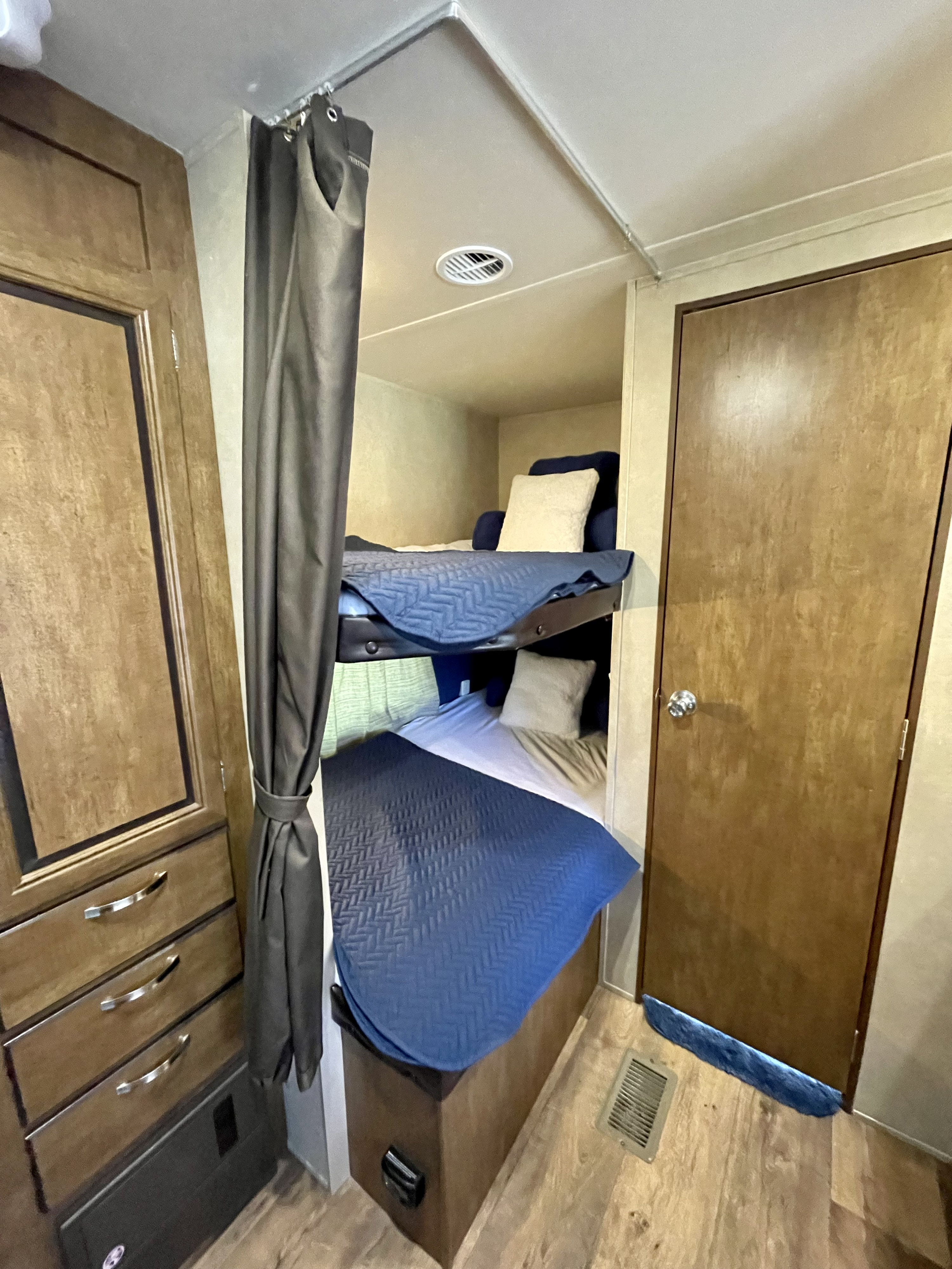 RV rental interior featuring cozy bunk beds with a privacy curtain, adjacent storage, and a nearby access door.. Forest River Wildwood 2016