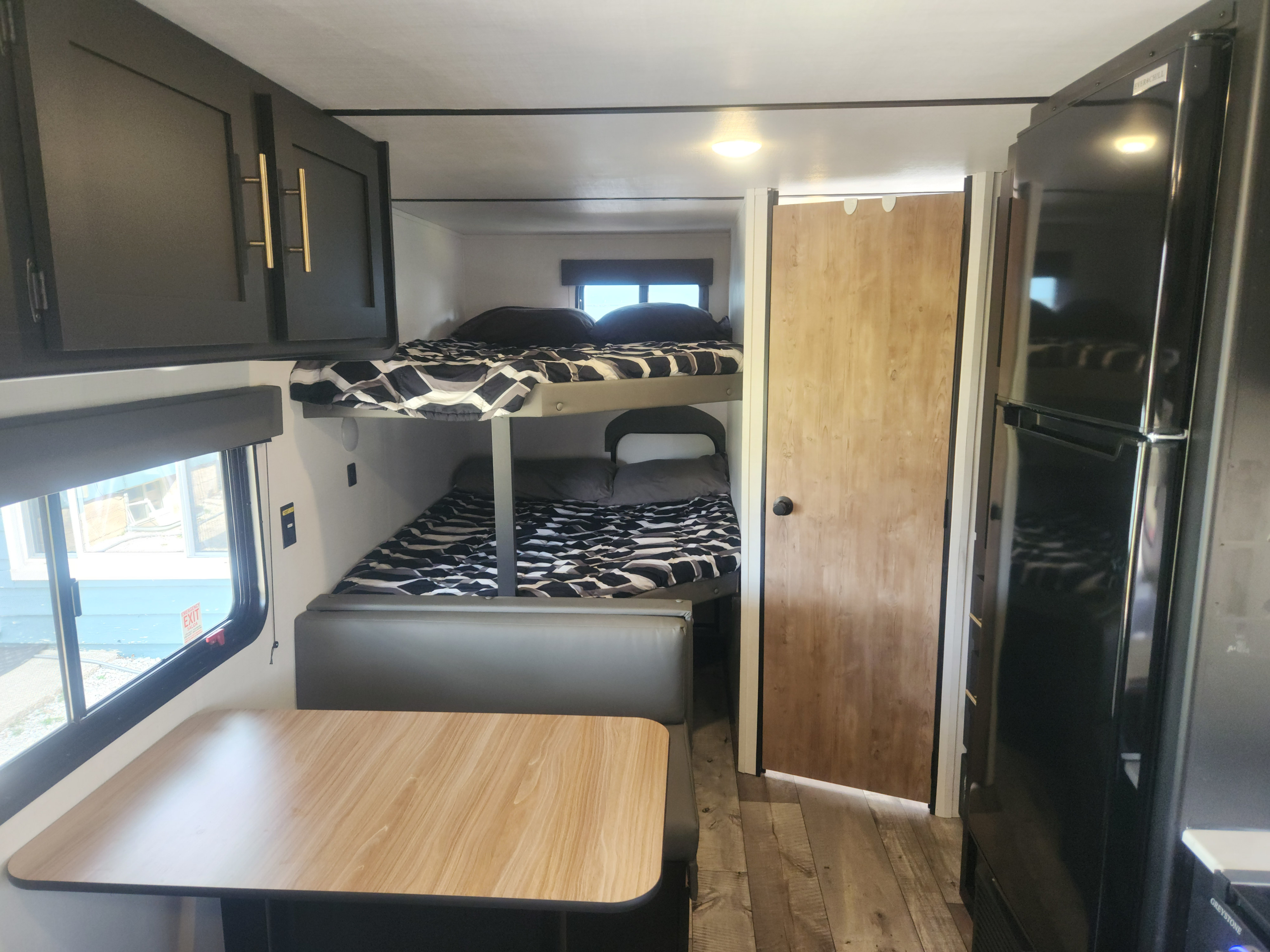 RV rental interior featuring a modern dining area, bunk beds, and kitchen with black cabinets and gold handles.. Keystone RV Springdale 2023