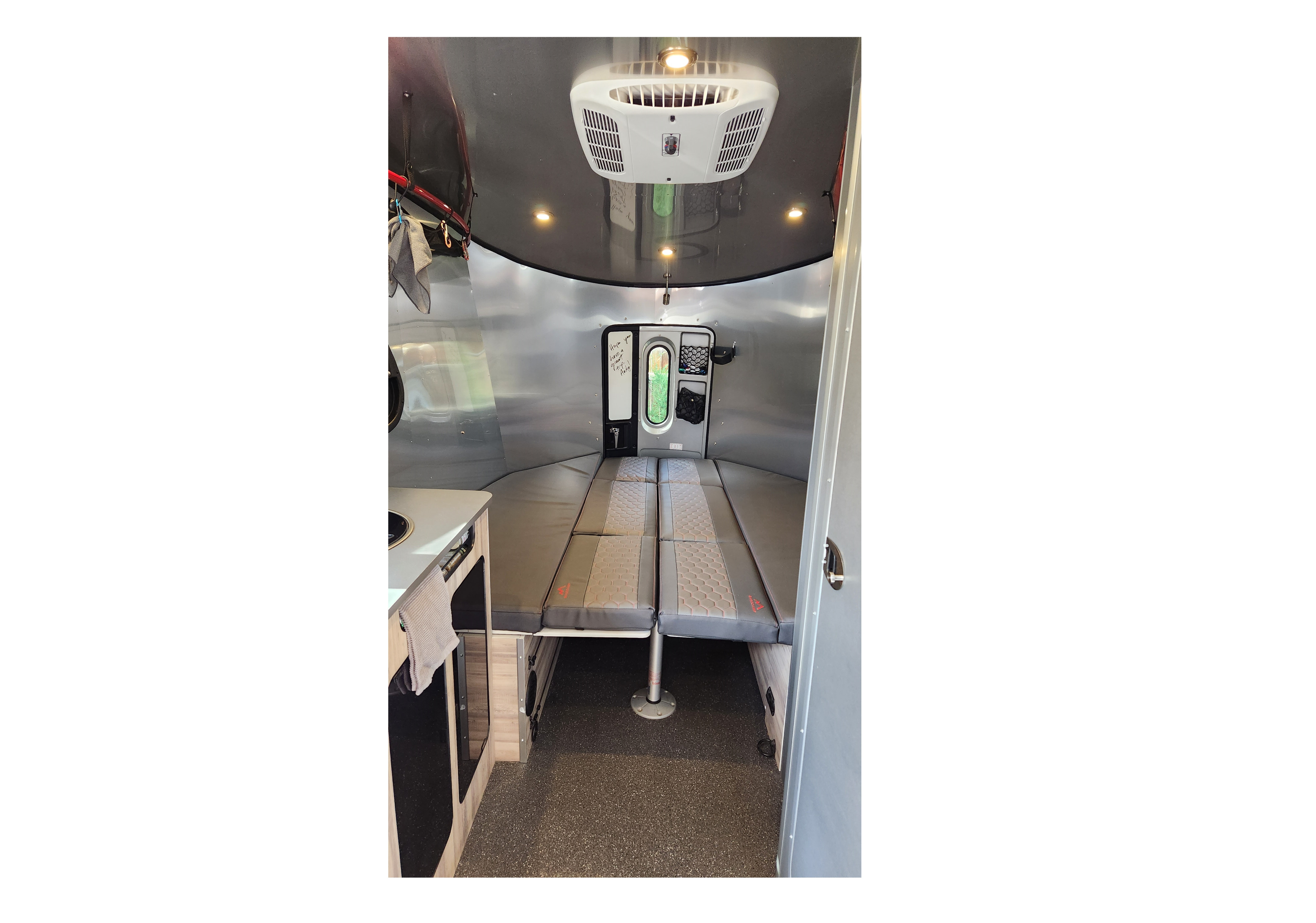 This rv rental interior features a convertible bed, small kitchen, AC unit, and compact living space for adventures.. Airstream Basecamp 2021