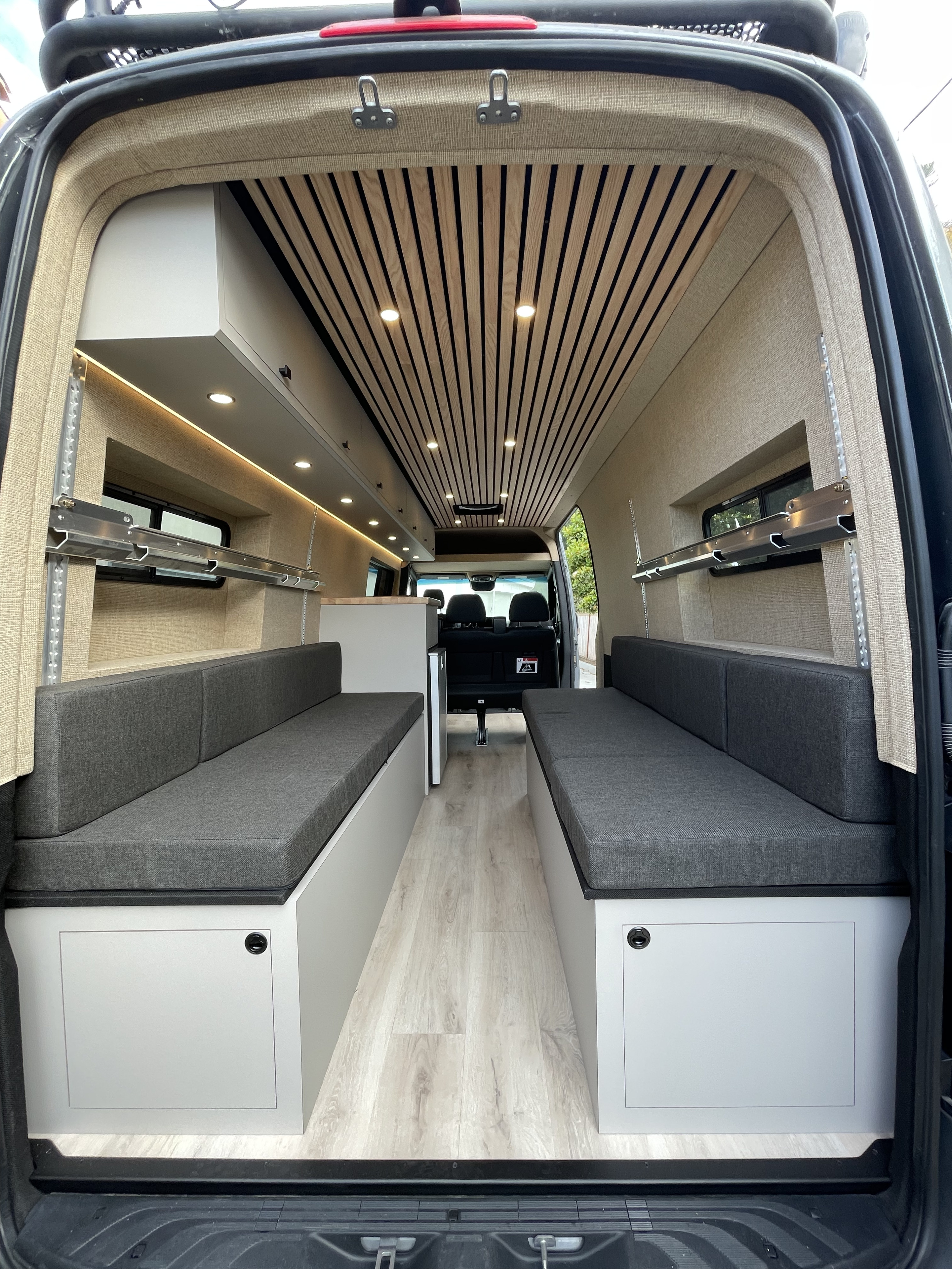 View inside a modern RV rental camper van: light wood ceiling, grey seating benches, and built-in storage. Ideal for travel.. Mercedes-Benz Sprinter 2020
