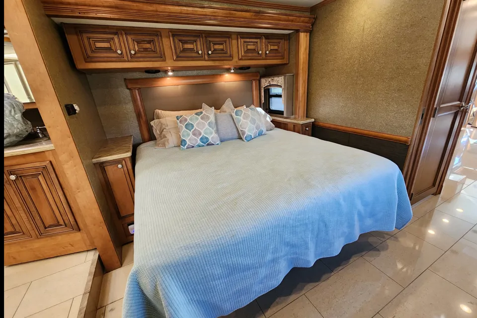 Cozy RV rental bedroom with a light blue bed, wooden cabinets, and accent lighting.. Thor Tuscany 2014