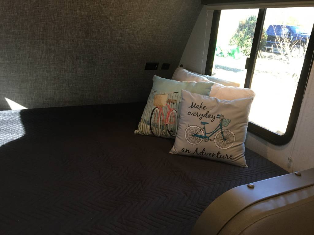 Cozy RV rental bedroom with bicycle-themed pillows, a bed, and a large window offering a view outside.. Winnebago Minnie Winnie 2021