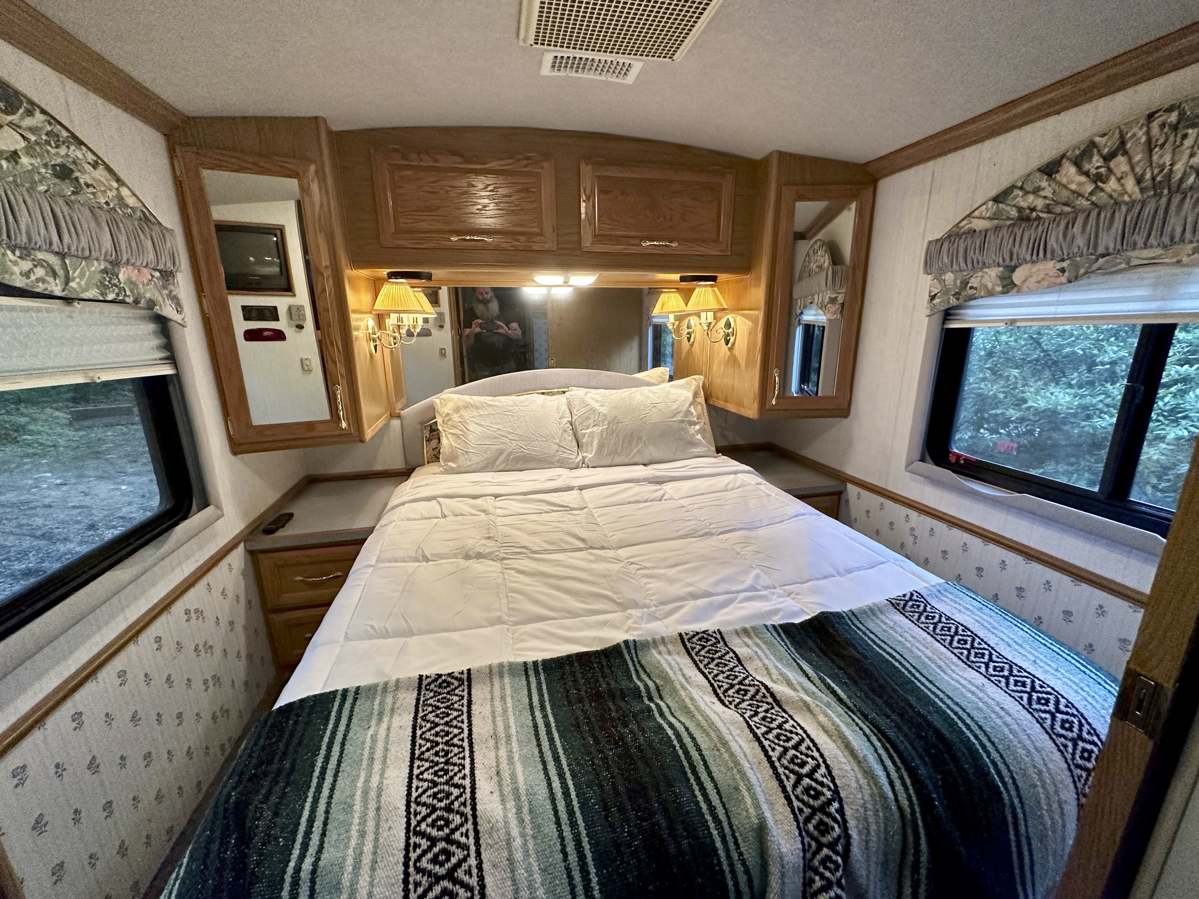 Comfortable RV rental bedroom featuring a spacious bed with cozy blanket, wooden storage, and windows. Ideal for travel.. Fleetwood Pace Arrow 1997