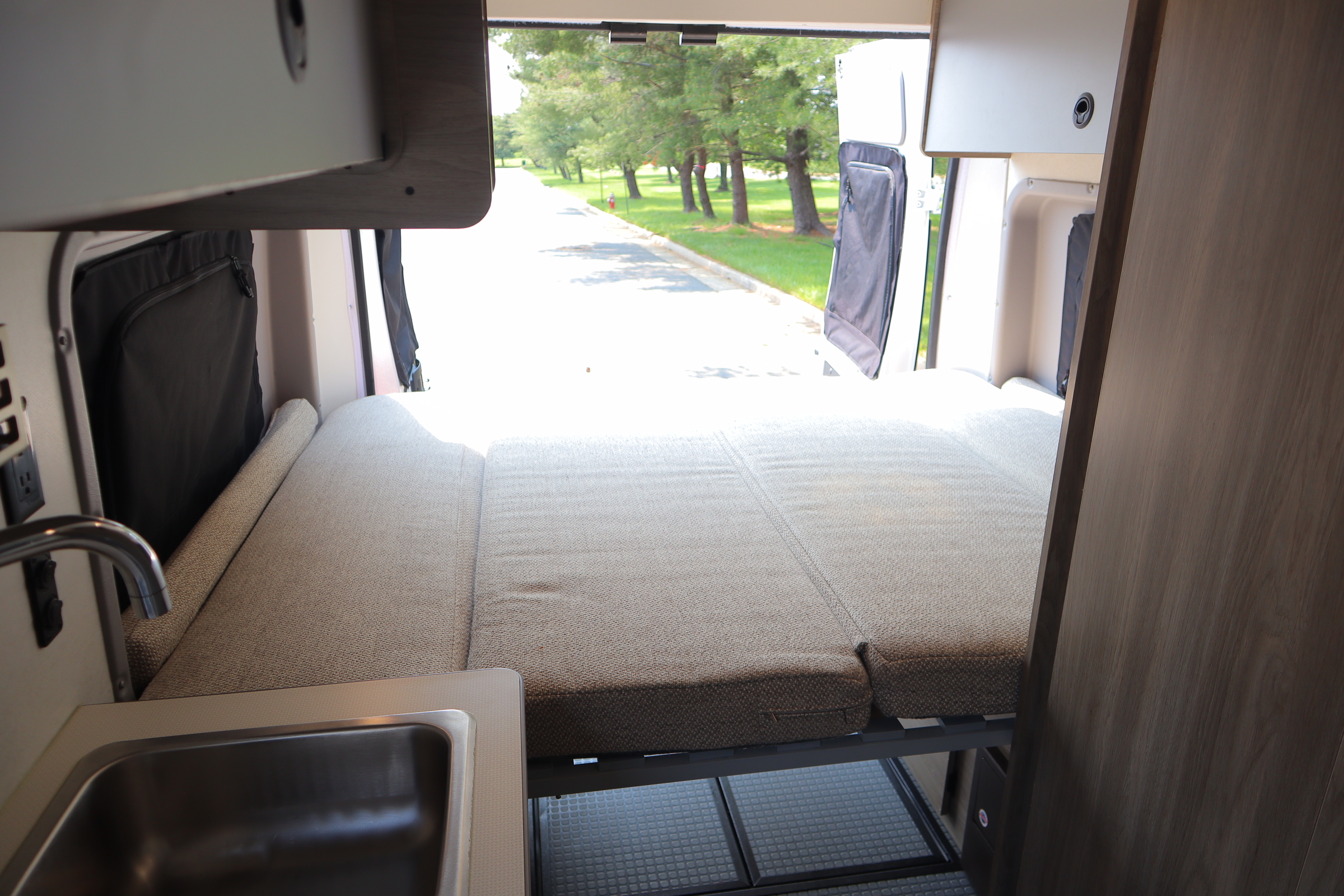 RV rental interior features a versatile bed, compact kitchen sink, and scenic rear view for adventurers.. Winnebago Solis 2021
