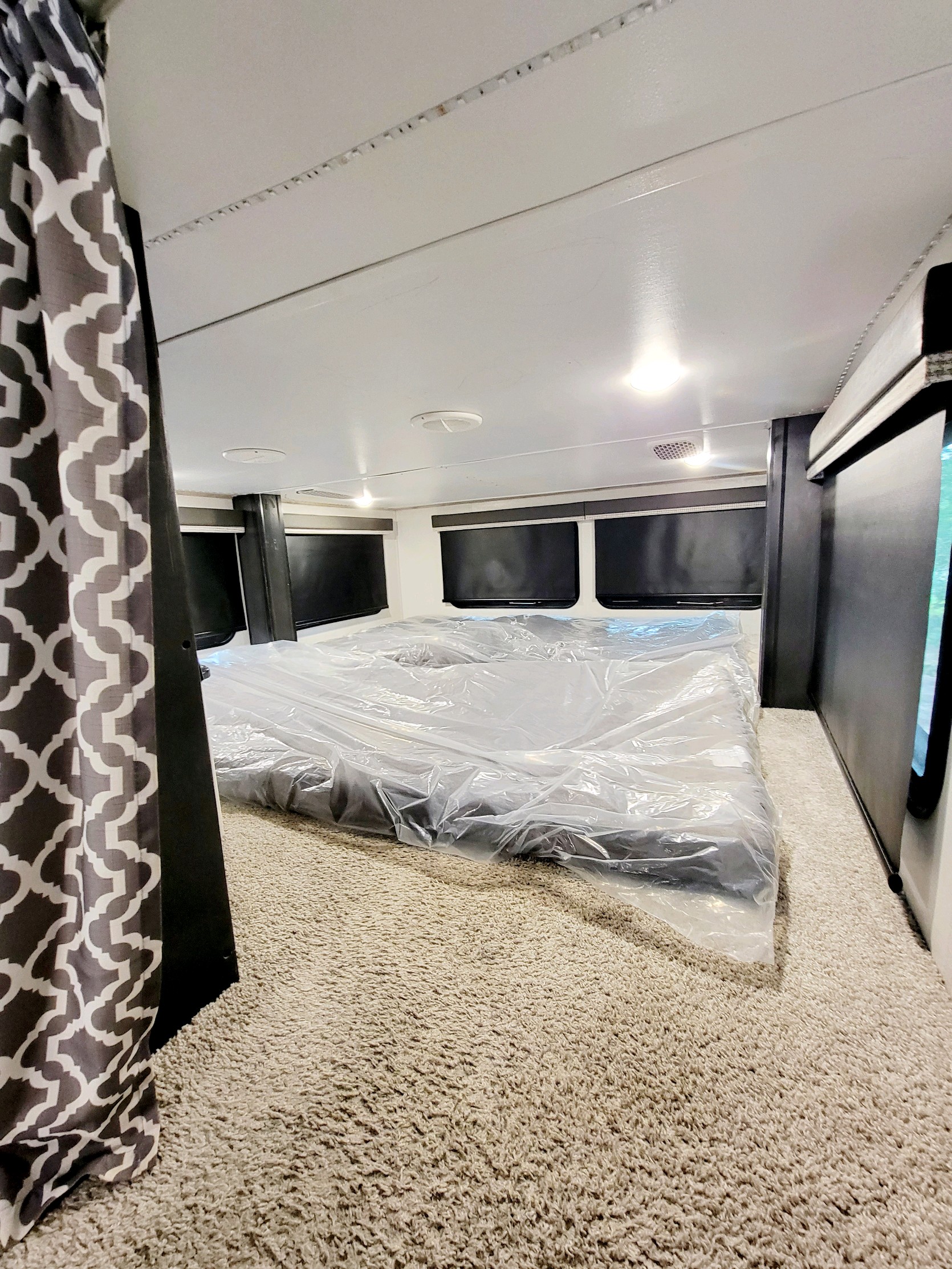 Inside a comfortable RV rental bedroom, featuring a new bed wrapped in plastic, roller blinds, and soft carpet.. Keystone Avalanche 2021