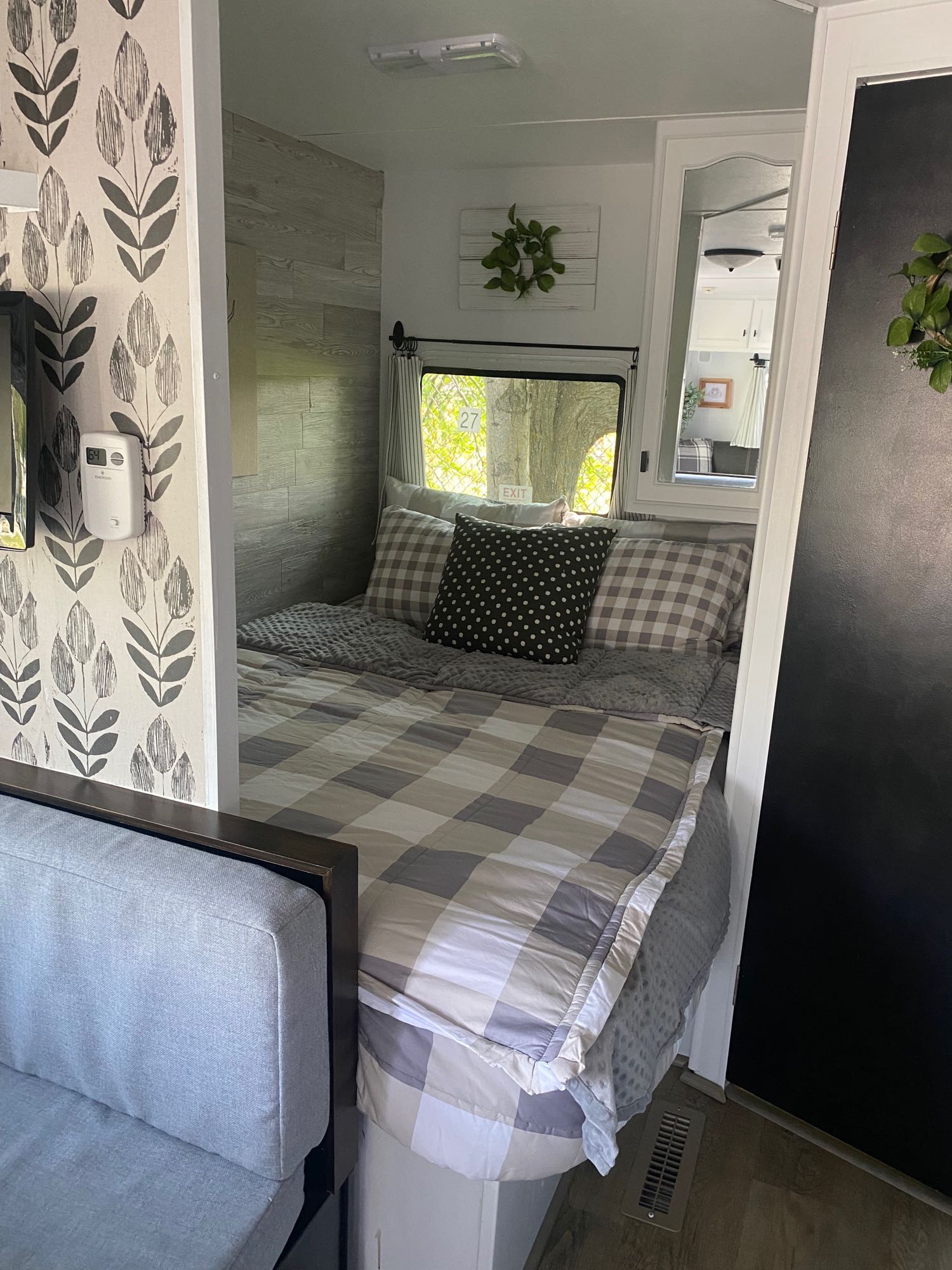RV rental interior: A cozy bedroom space with grey and white checkered bedding, a patterned wall, and a view outside.. Dutchmen Lite 2007