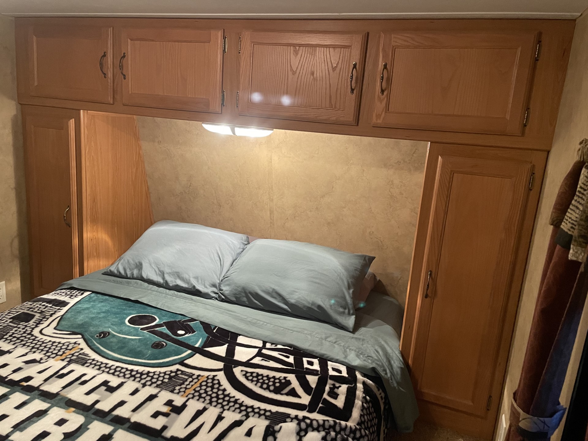 An RV rental bedroom with a bed, light blue bedding, overhead cabinets, side wardrobes, and a bright reading light.. Keystone Hideout 2009