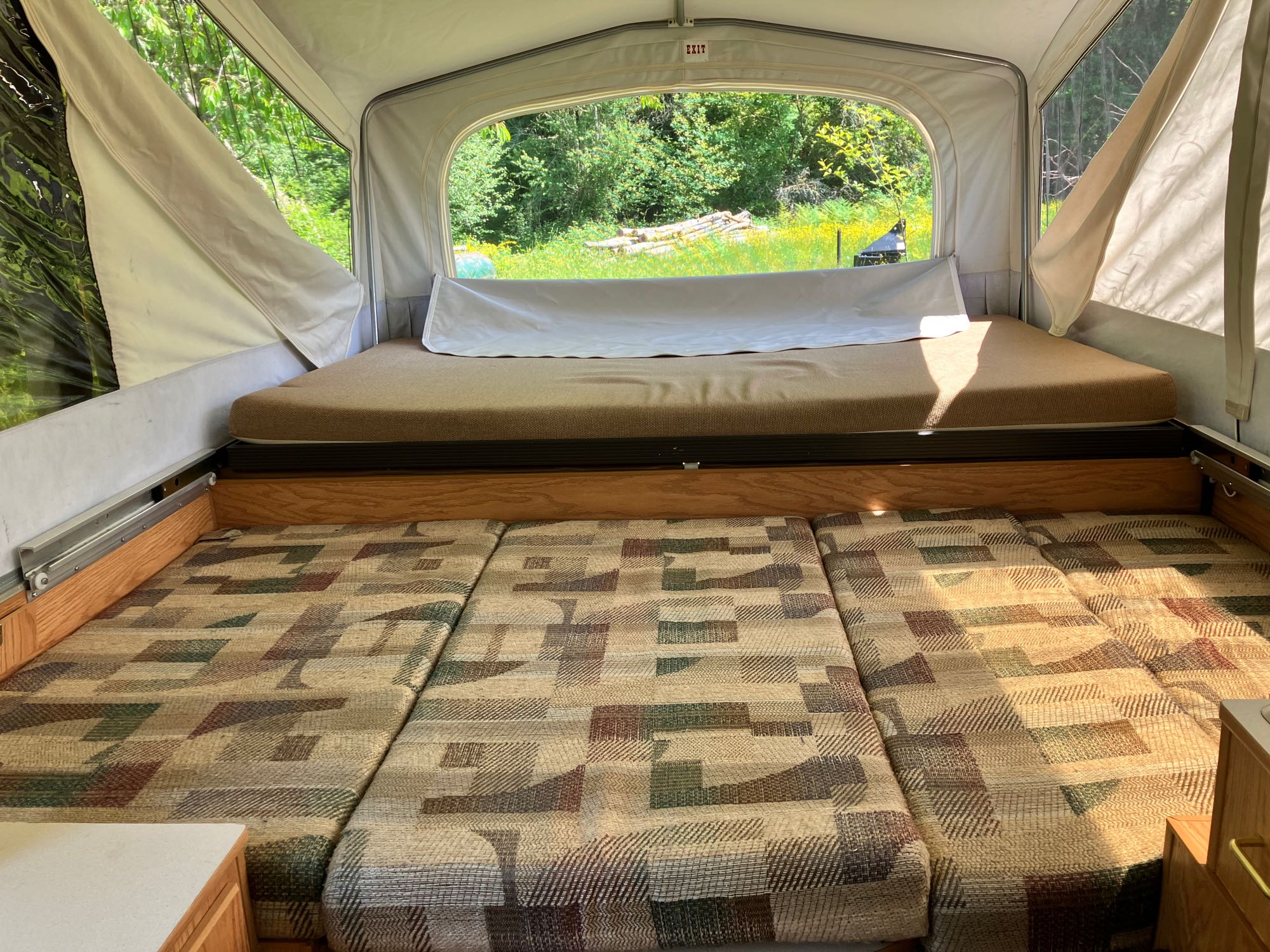 Inside a cozy pop-up RV rental: Two sleeping areas, patterned cushions, and a large window view of nature.. Jayco Qwest 2003