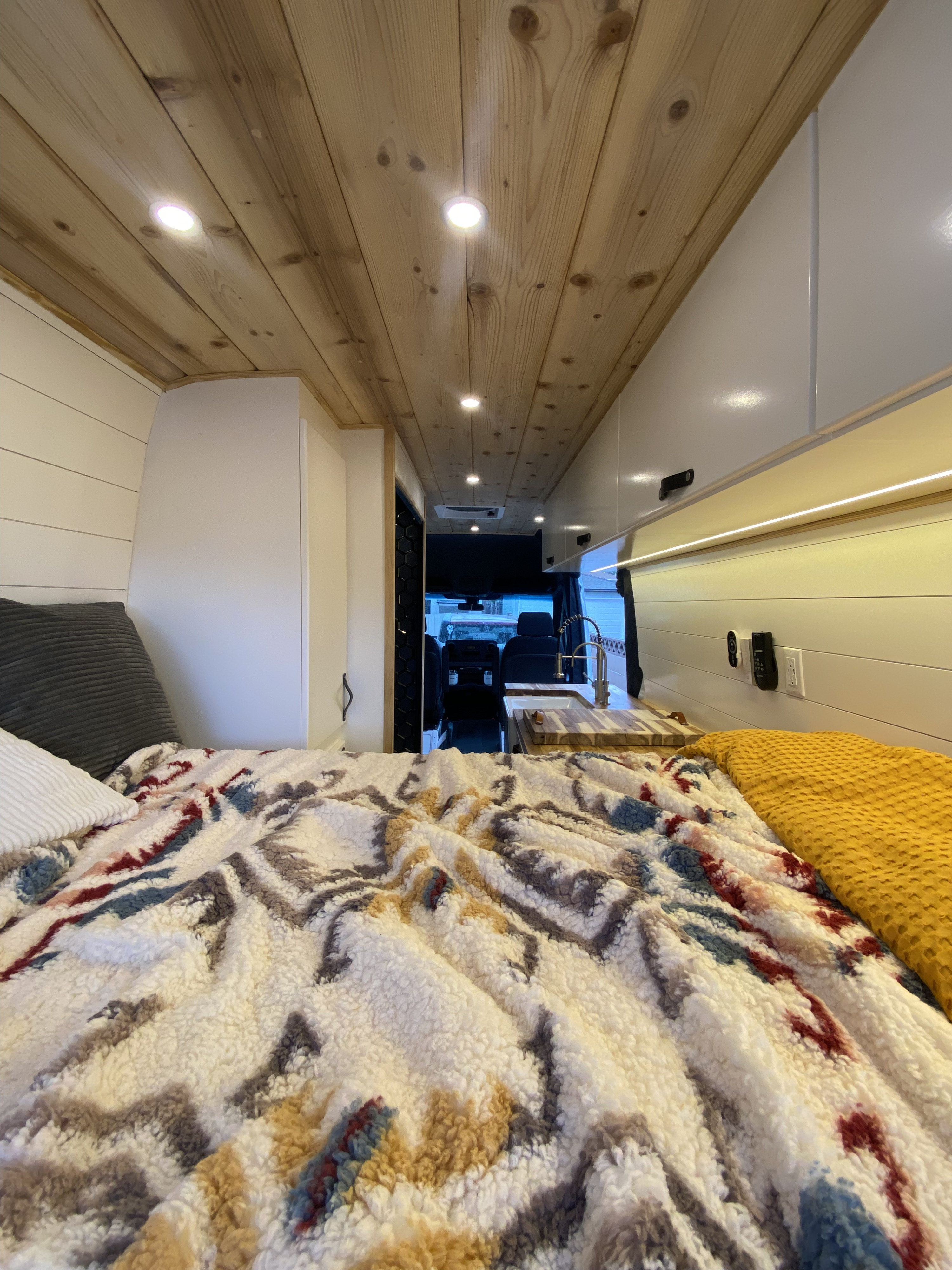 Cozy RV rental interior with a comfortable bed, warm wood ceiling, and compact kitchen.. Mercedes-Benz Sprinter 2022