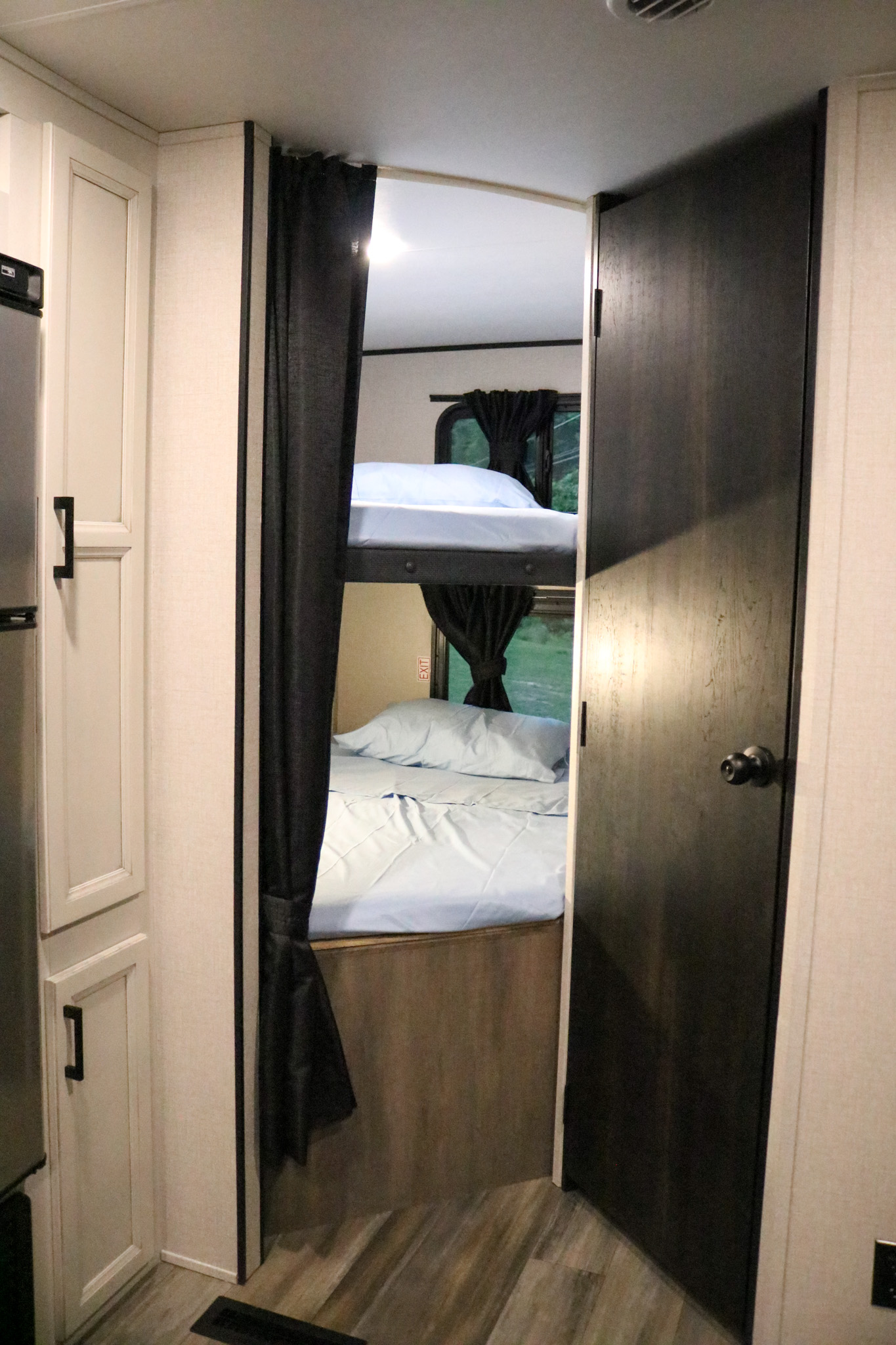 This RV rental shows cozy bunk beds with light blue sheets behind a dark privacy curtain, perfect for family trips.. Highland Ridge RV Open Range 2023