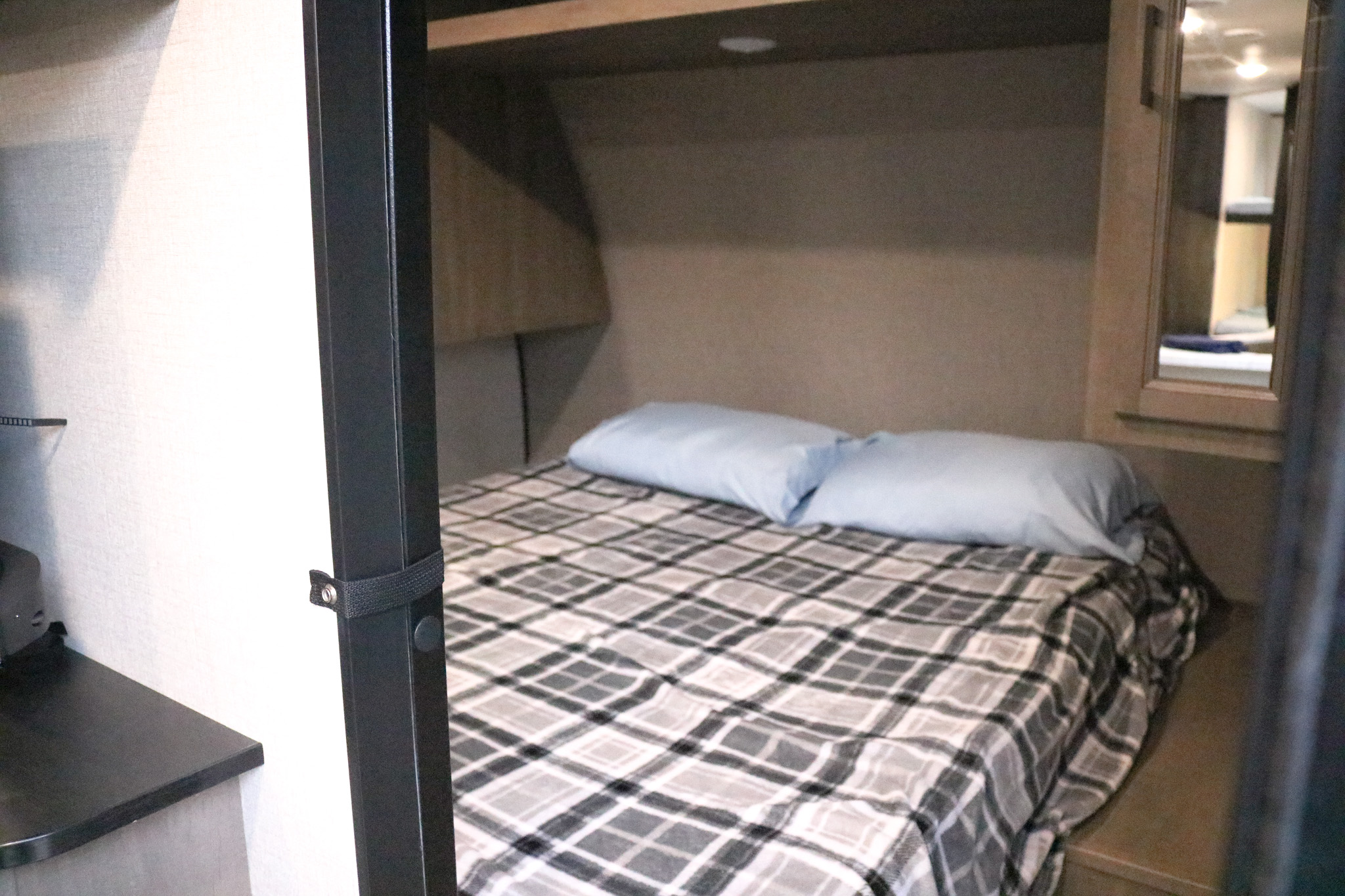 Cozy RV rental bedroom with a plaid blanket, light blue pillows, and overhead storage. Ideal for comfortable travel.. Highland Ridge RV Open Range 2023