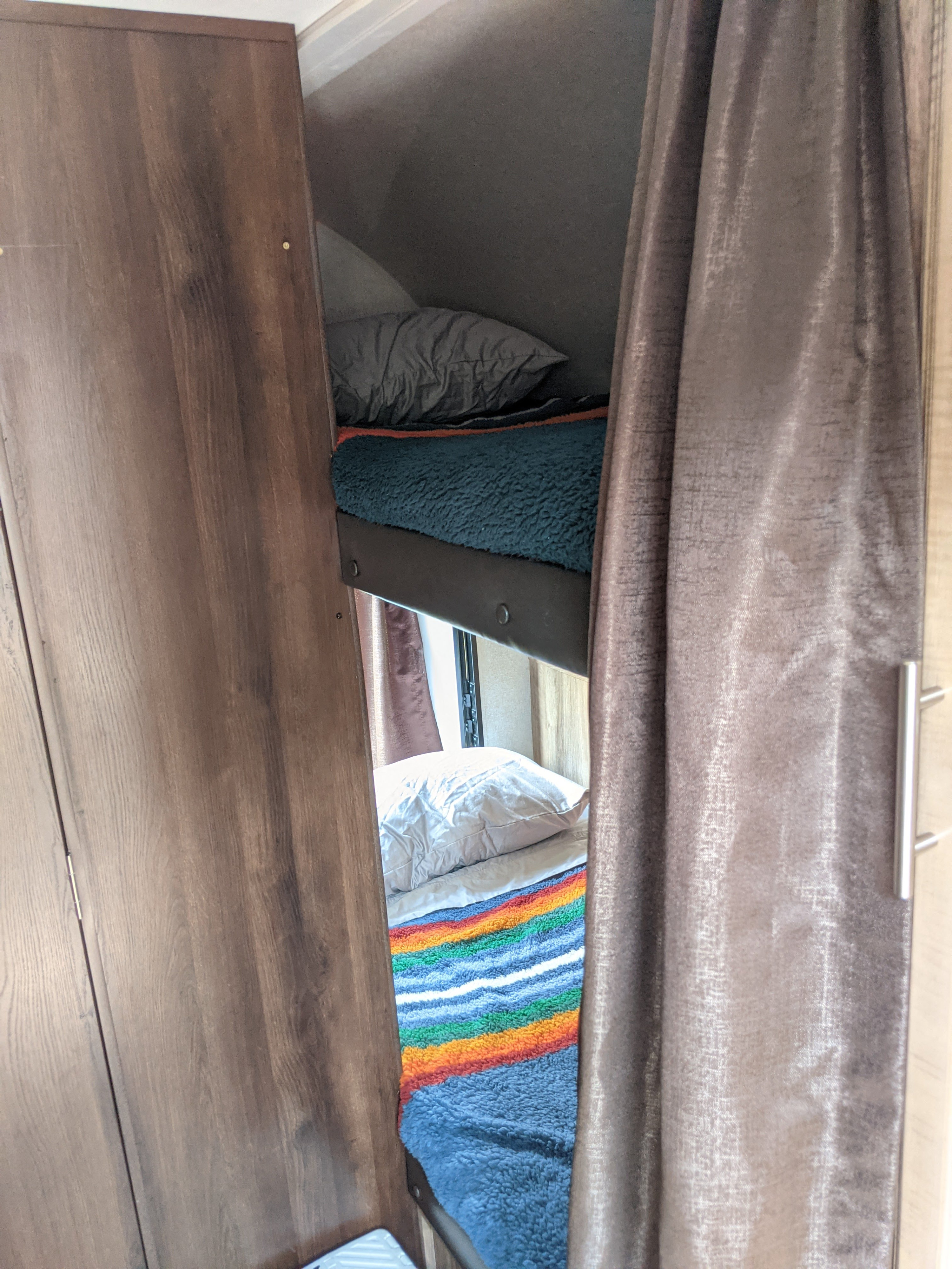 Cozy rv rental bunk beds, ready for rest. Top bunk has a teal blanket, bottom a vibrant rainbow stripe, framed by wood and curtains.. Jayco Jay Feather x213 2019