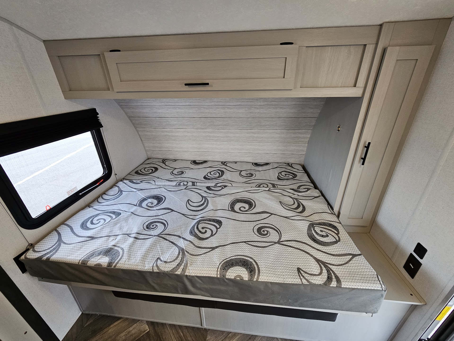 RV rental bedroom interior featuring a bed with patterned mattress, overhead cabinets, and a window.. Forest River Wildwood FSX 2021