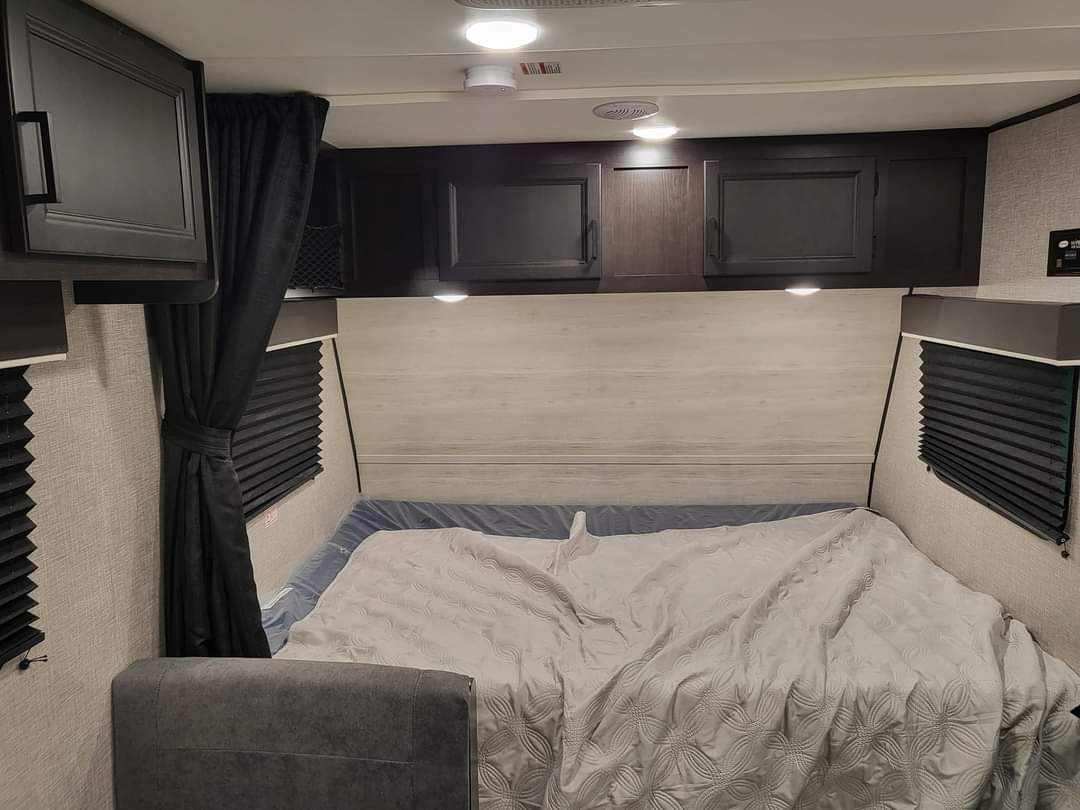 Explore this RV rental's cozy bedroom. It features a bed, overhead cabinets, and pleated window blinds.. Jayco Jay Flight SLX 2022