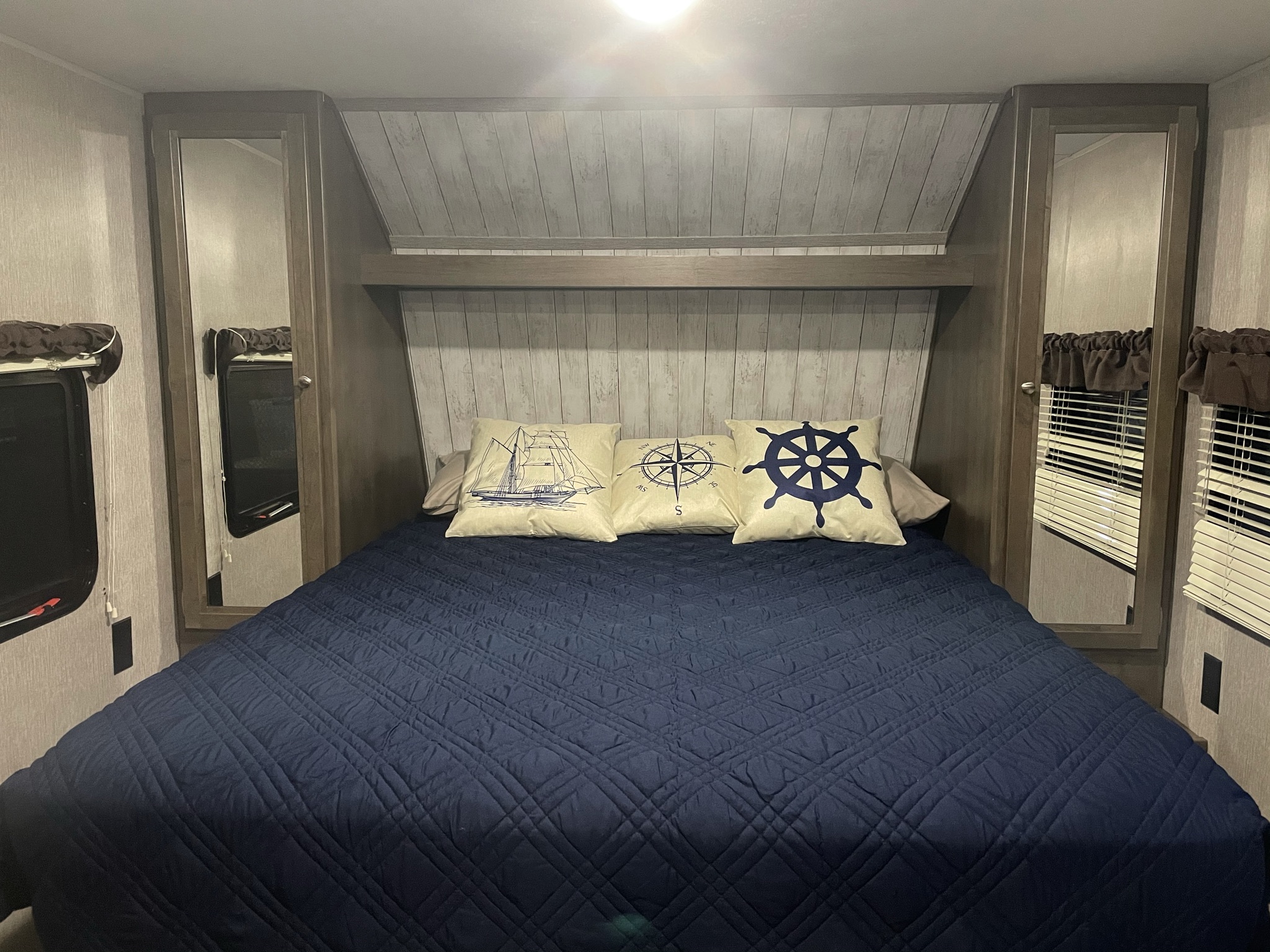 Cozy RV rental bedroom features a navy quilted bed with nautical-themed pillows and mirrored closets.. Dutchmen Coleman Lantern LT 2019