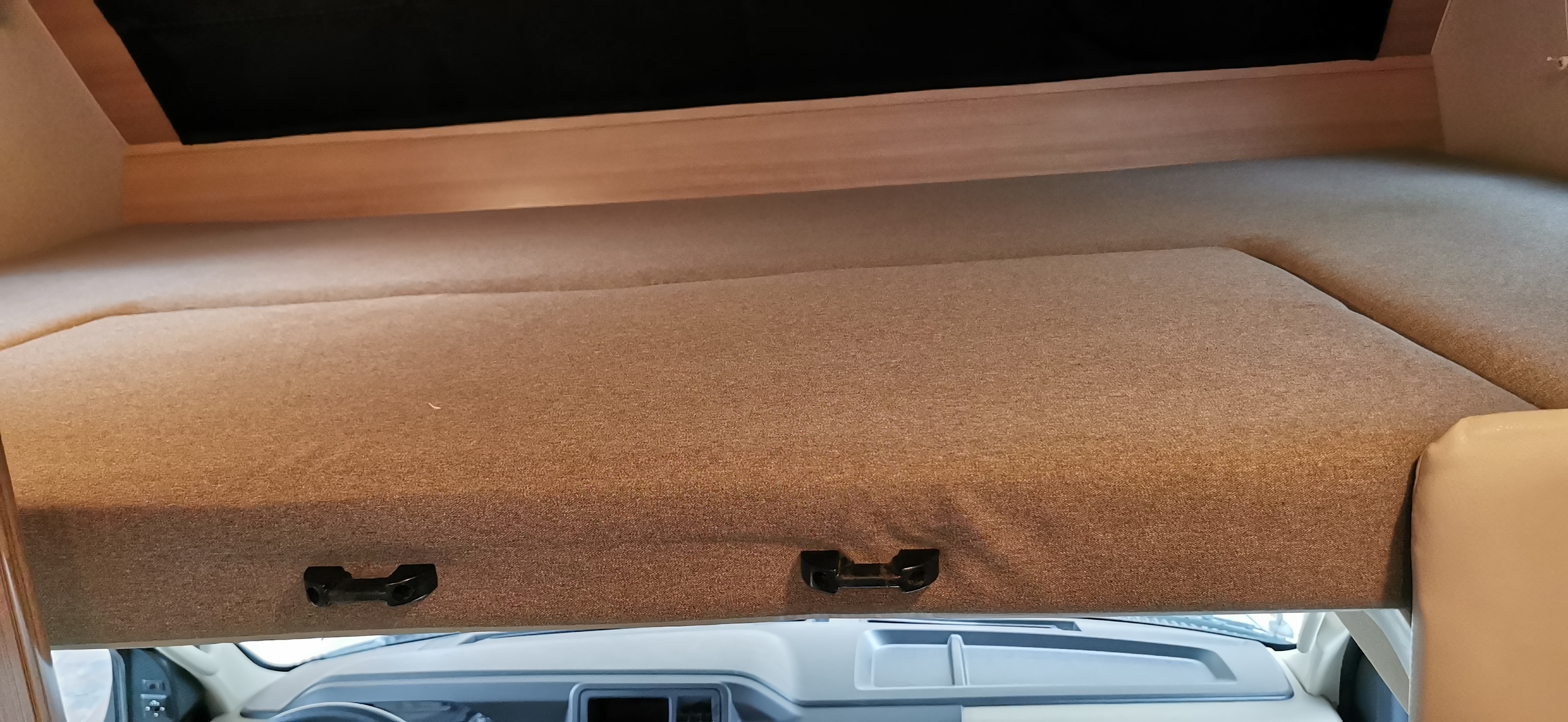 Inside an RV rental: the tan, upholstered cab-over bunk bed, with the vehicle's dashboard below.. Ford Adventure 2021