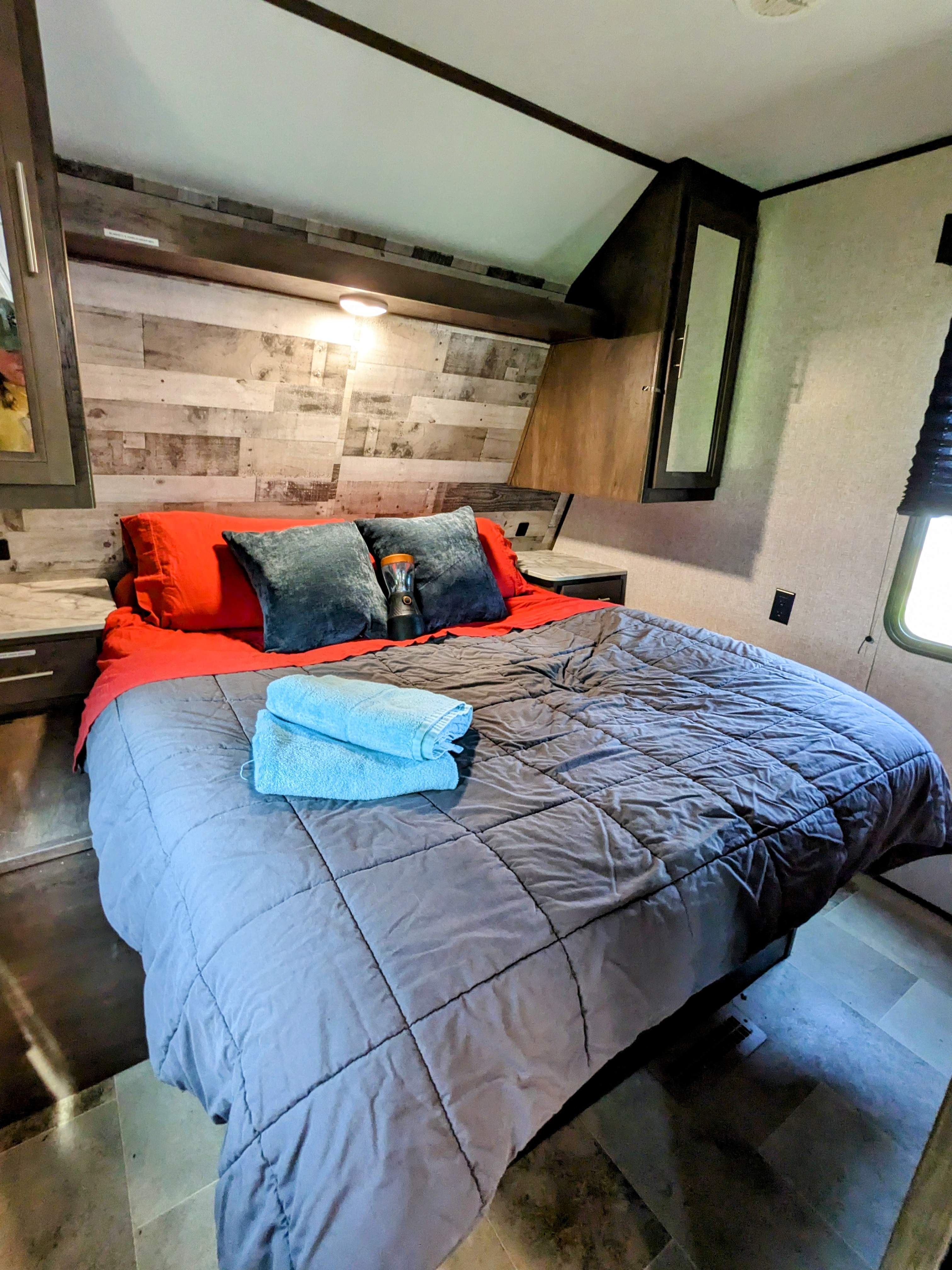 Cozy RV rental bedroom with queen bed, wood paneling, overhead cabinets, and fresh towels for a comfortable stay.. Coleman Lantern 2021
