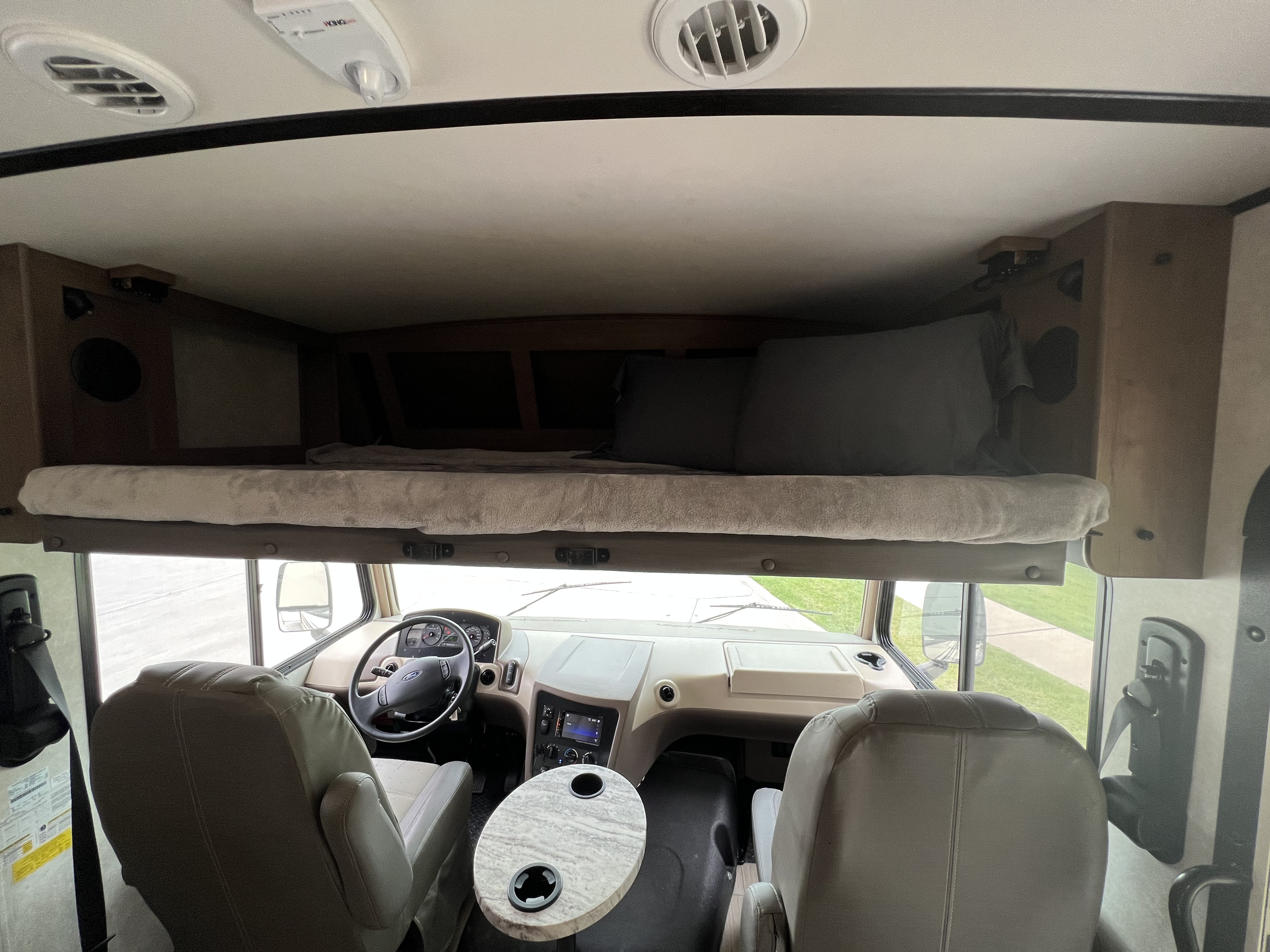 An RV rental's cockpit, featuring a steering wheel, seats, a small table, and an overhead bunk bed.. FR3 FR3 Motorhome 2021