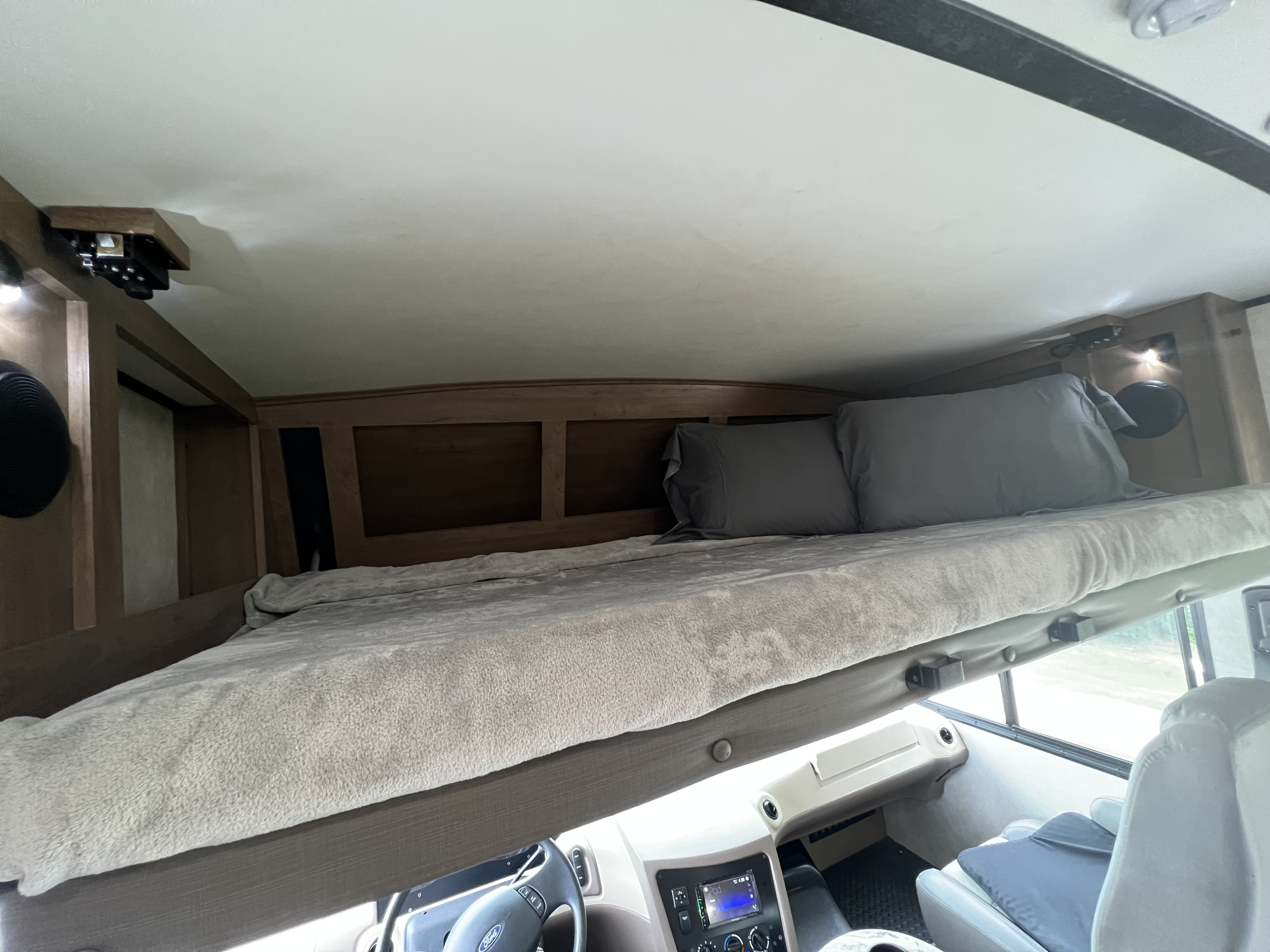 Cozy RV rental over-cab bunk bed with pillows and blanket, showing the front interior and dashboard below.. FR3 FR3 Motorhome 2021