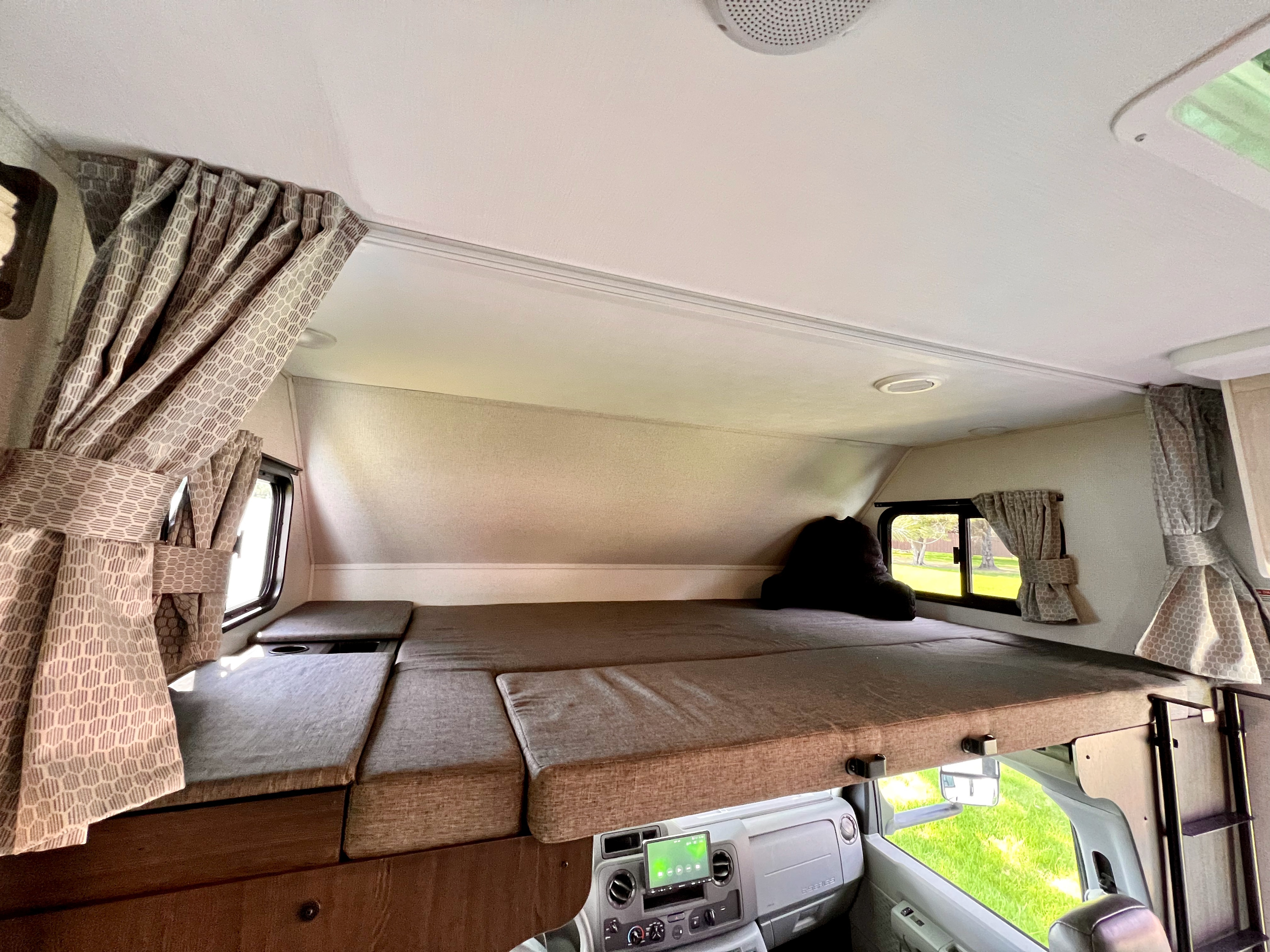 Explore this RV rental's spacious cab-over bunk bed, featuring comfy cushions, side windows, and stylish curtains.. Forest River Sunseeker Classic 2021