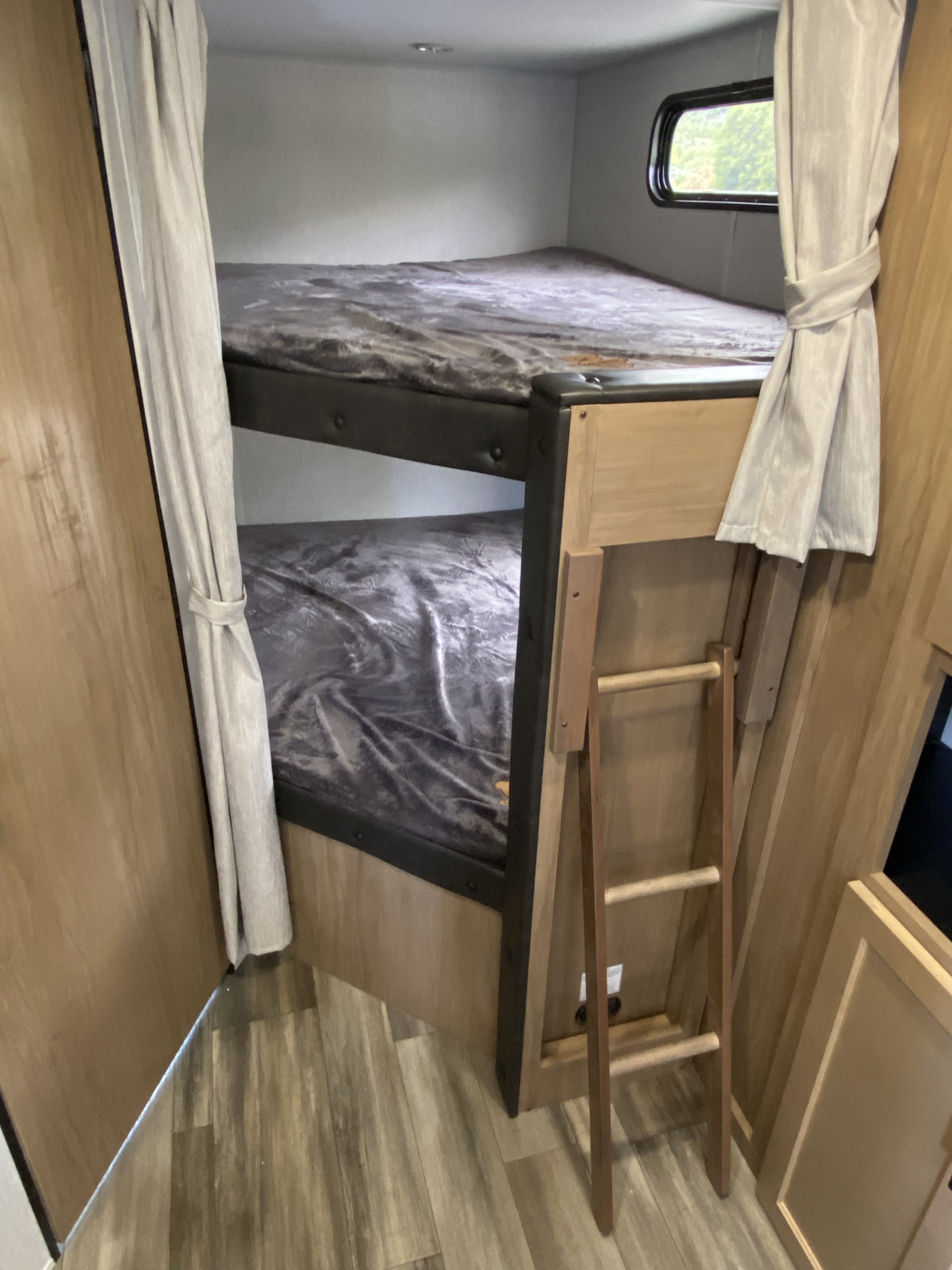 Inside an rv rental: cozy bunk beds with gray bedding, a ladder, and light curtains. Perfect for family adventures.. Forest River 23DBH 2023