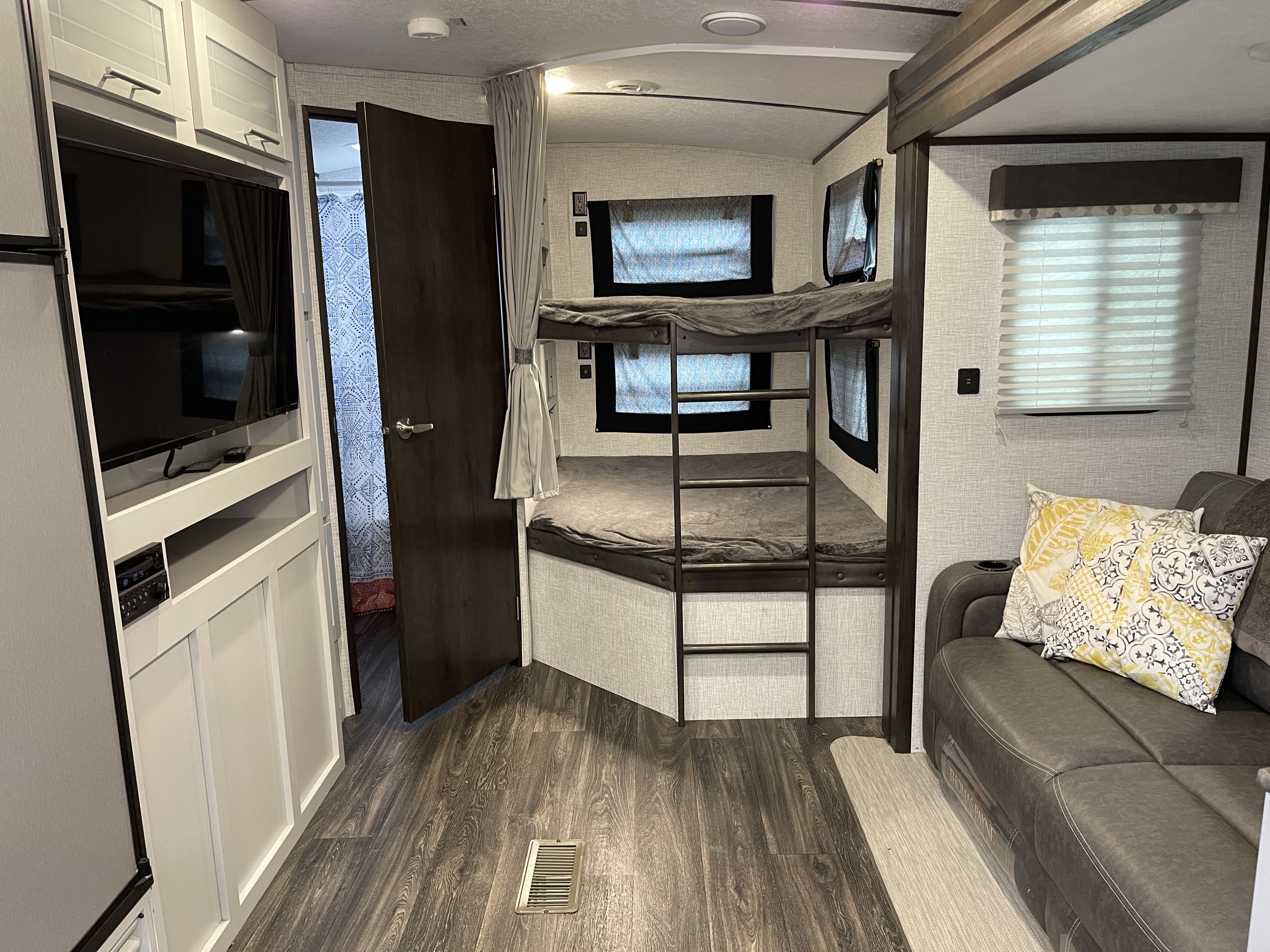Interior of an RV rental showing bunk beds, a comfortable sofa, TV, and storage cabinets, ideal for family trips.. Keystone RV Bullet Ultra Lite 2021