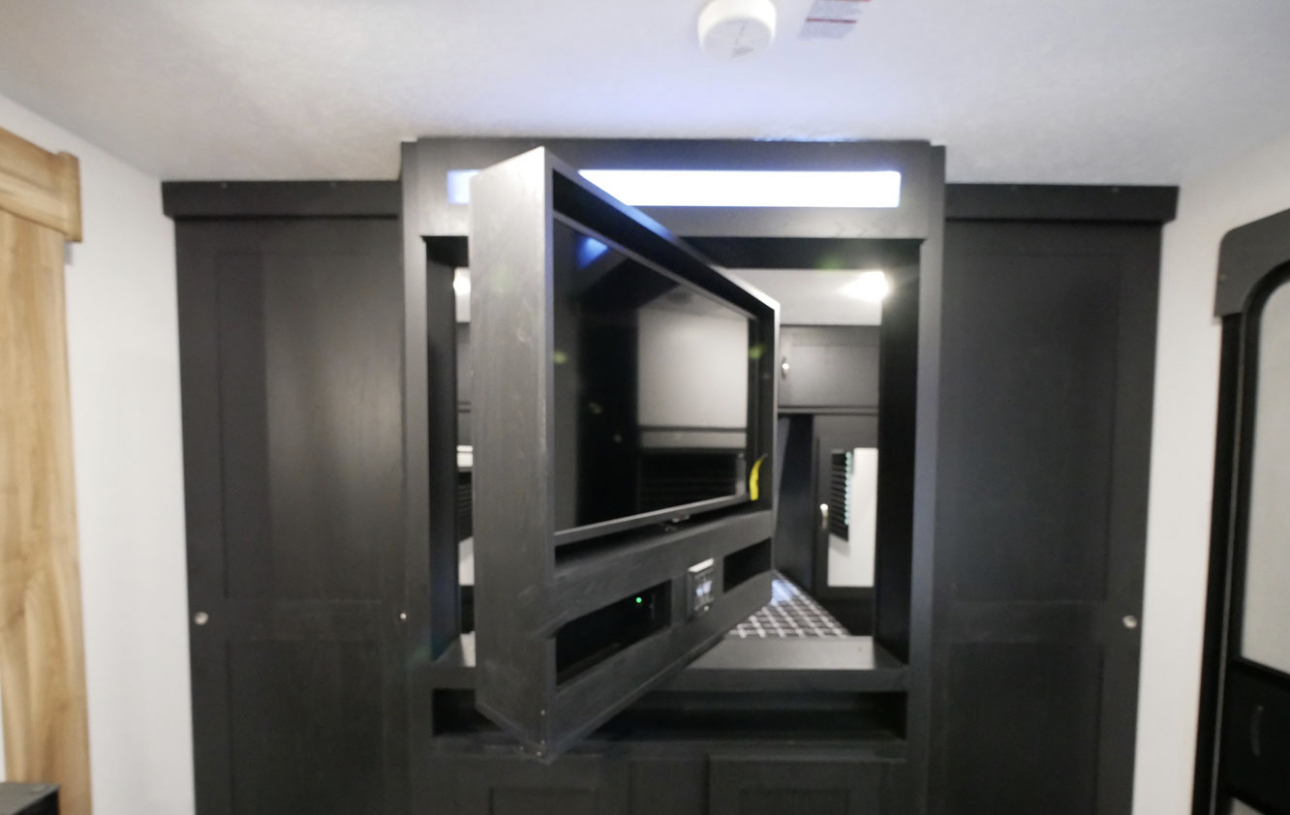 This RV rental interior features a black entertainment unit with a swiveling TV and adjacent dark sliding doors.. Coachmen 257BHS 2022