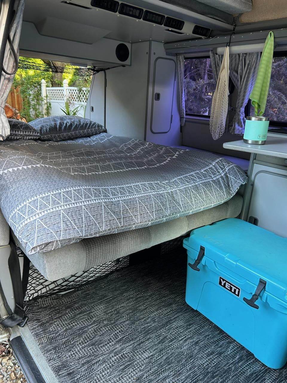 Cozy RV rental interior: a comfy bed, large blue YETI cooler, and essentials for your next van life adventure.. Volkswagen T3 Westfalia 1990