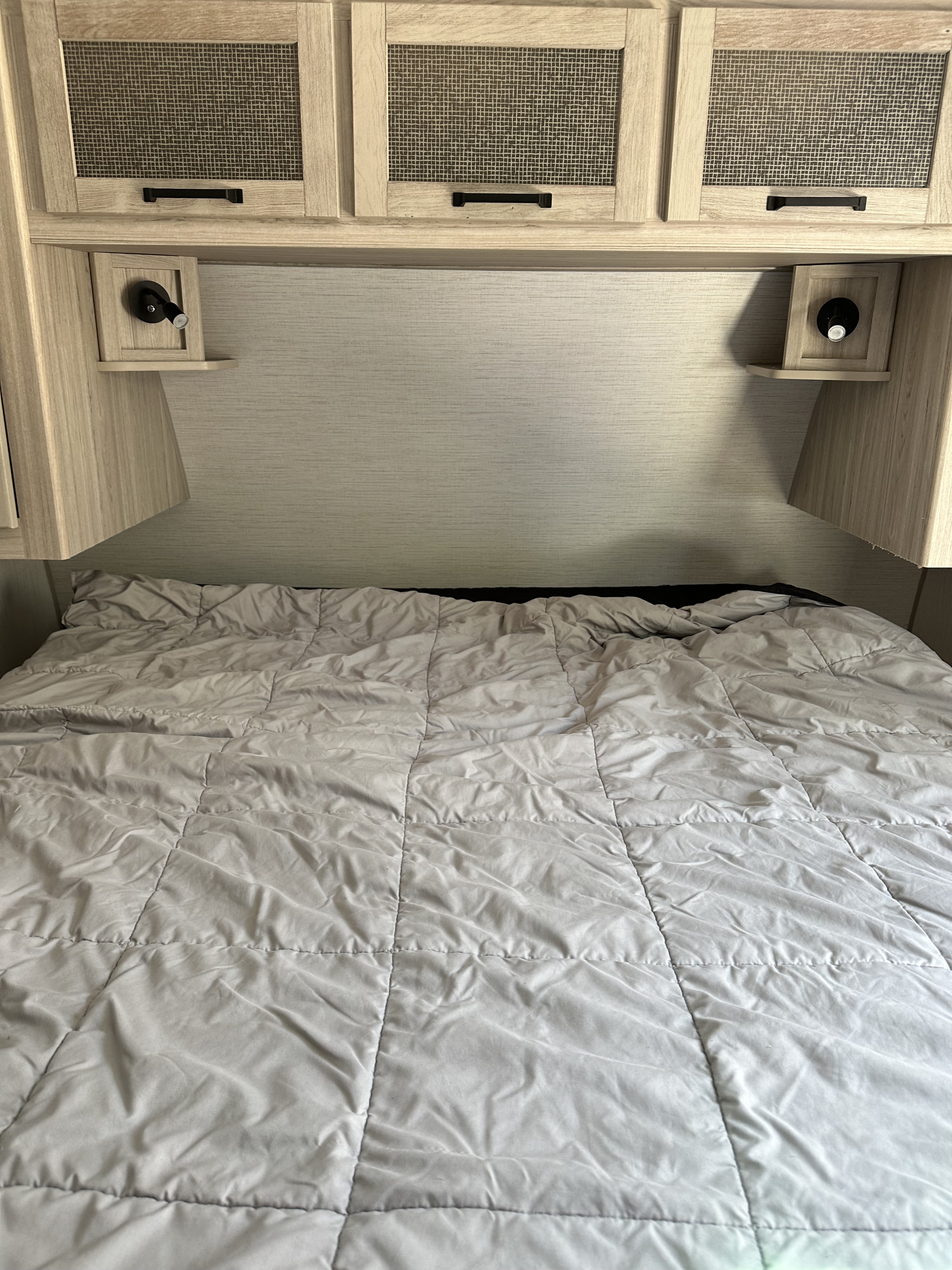 RV rental bedroom: a cozy bed with a grey comforter, overhead cabinets, and convenient reading lights above.. Twilight RVS Signature 2022