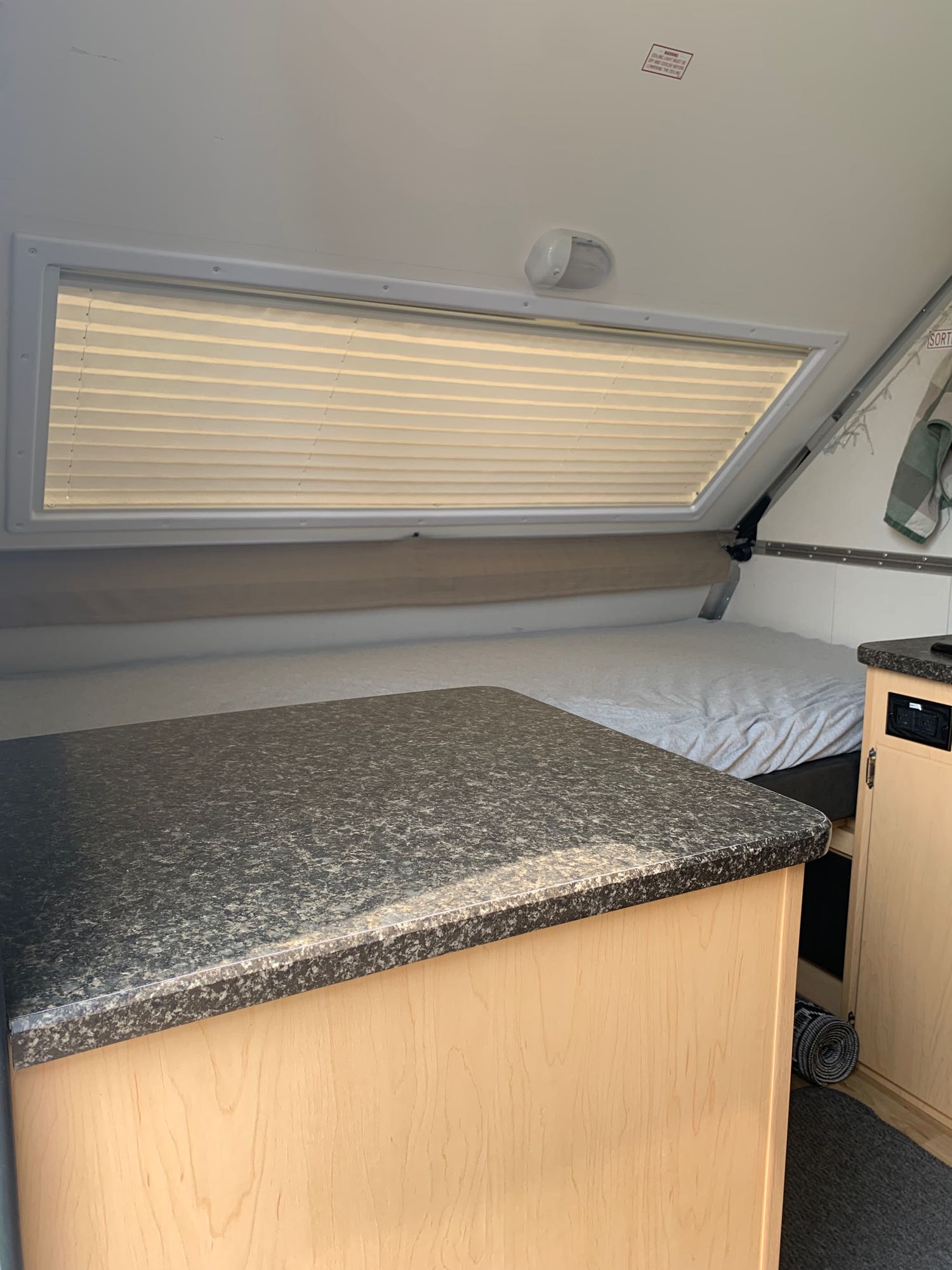 Inside an RV rental: a compact living space featuring a bed, dark counter, and window with blinds.. A Liner A Liner Popup Trailer 2020