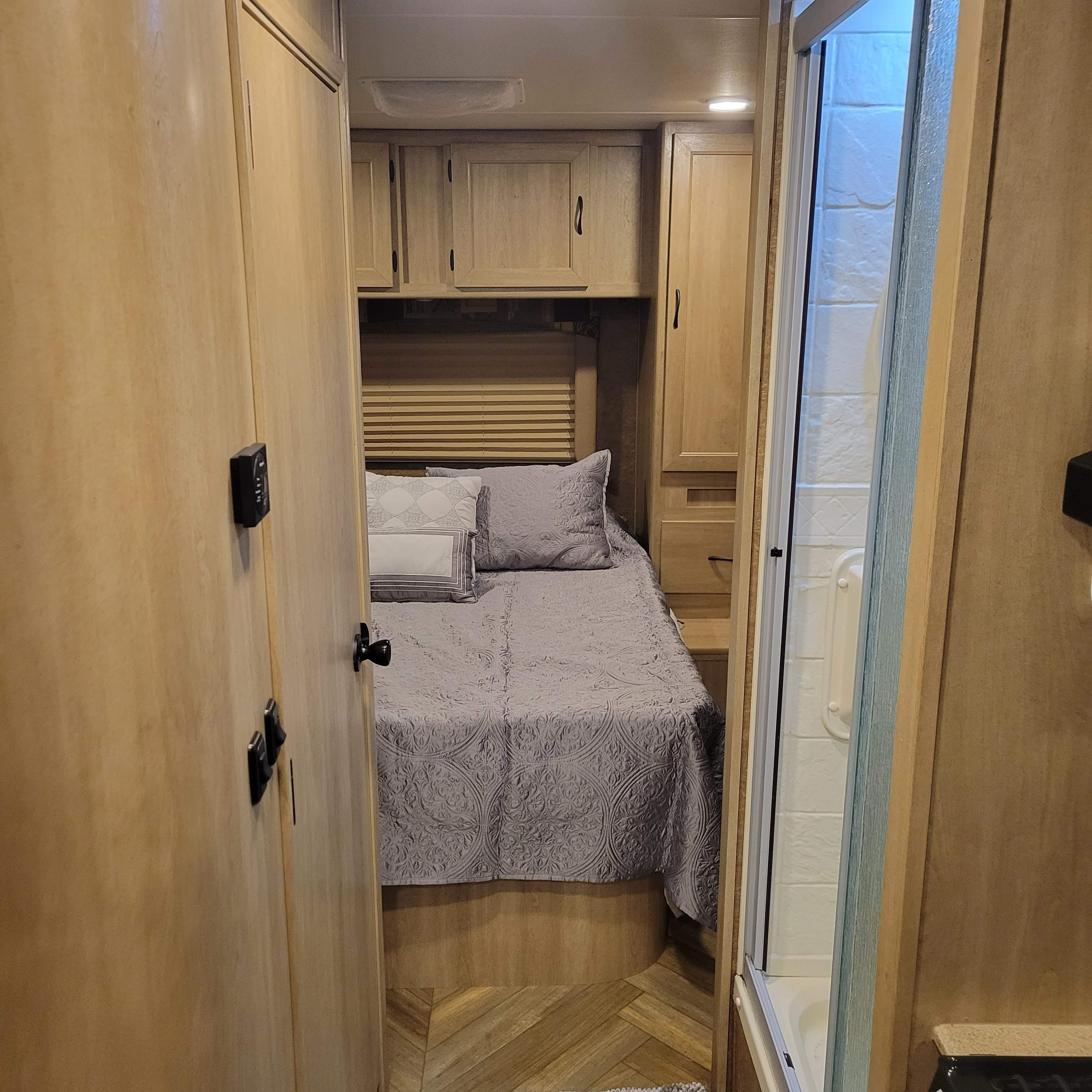 Inside an **rv rental**: a cozy bedroom with wood cabinetry and a shower on the right. Perfect for travel.. Forest River Coachmen Freelander 2016