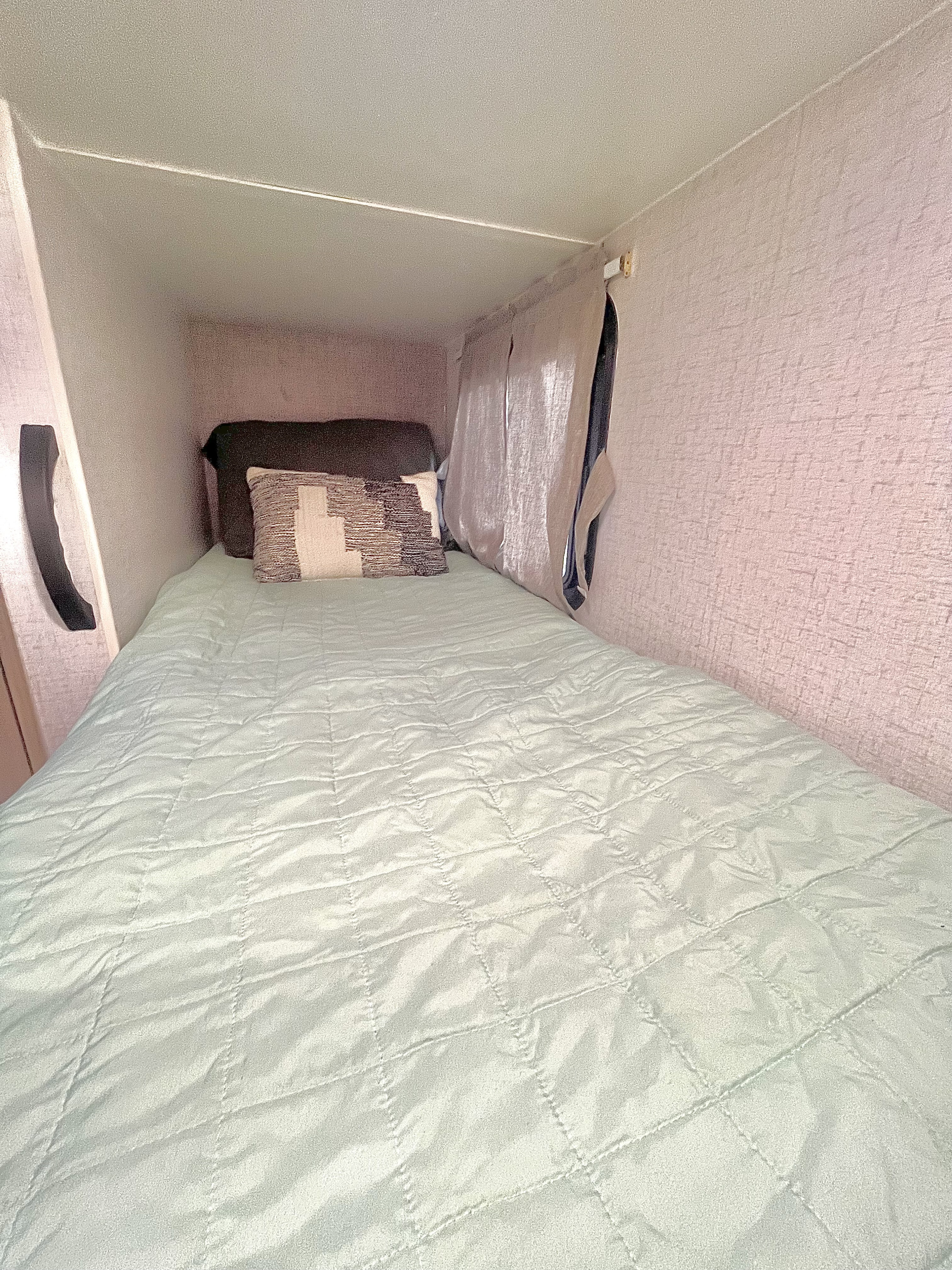 Inside an RV rental: a compact sleeping area with a mint green quilted bed, pillows, and window.. Winnebago Micro Minnie 2100BH 2022