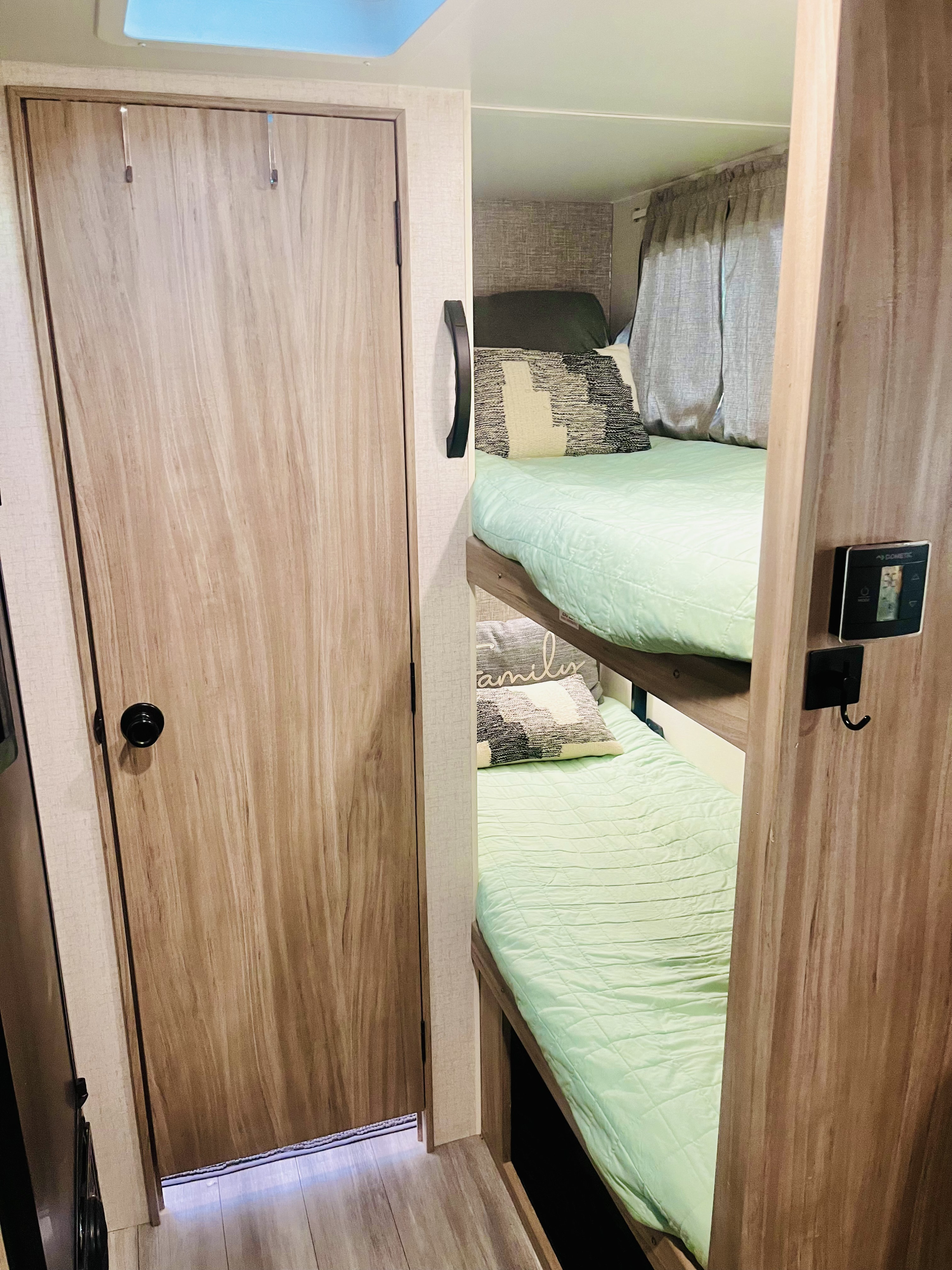 Cozy RV rental bunk beds with mint green bedding and decorative pillows, next to a wooden door and control panel, ideal for family trips.. Winnebago Micro Minnie 2100BH 2022