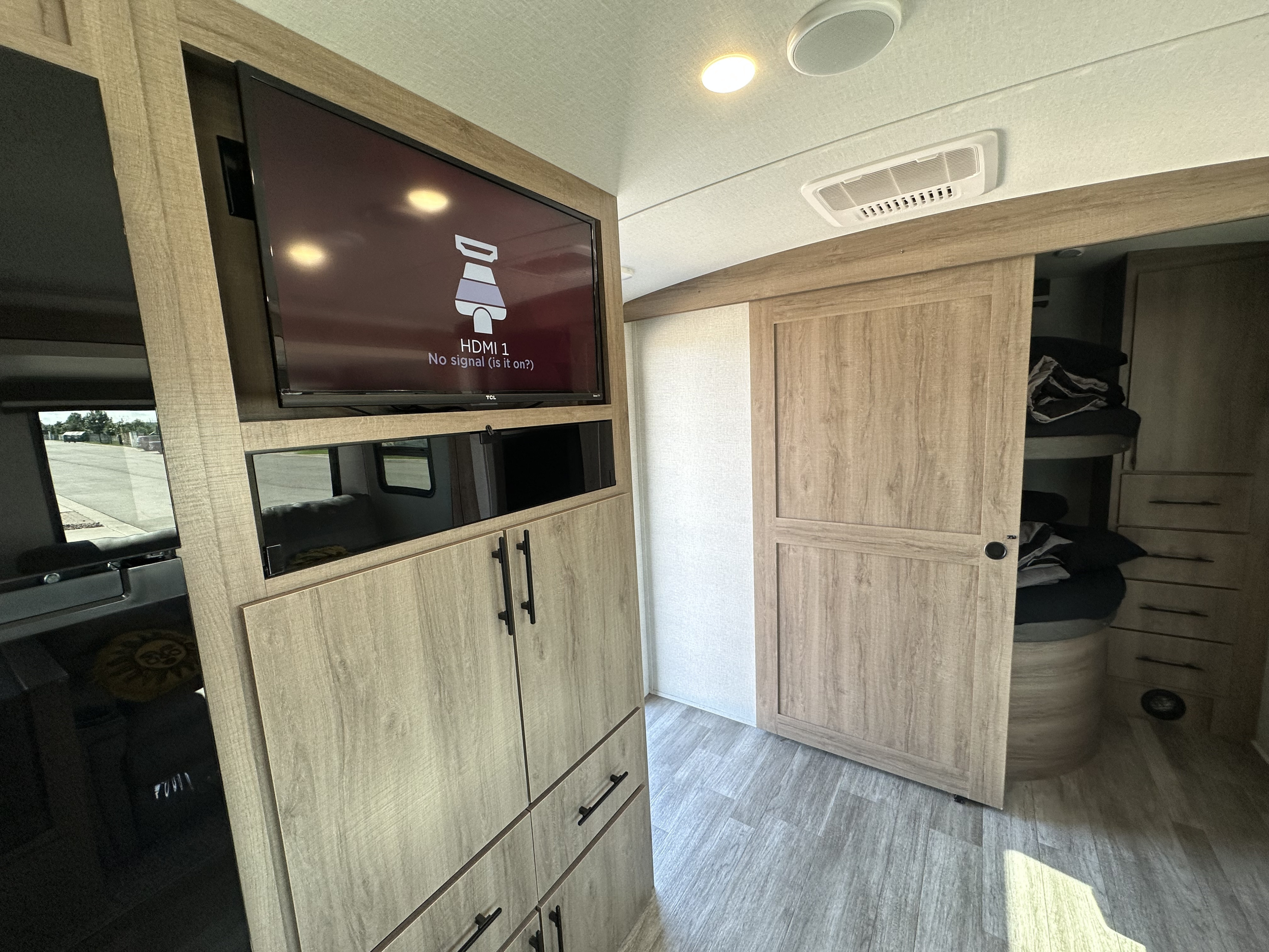 Inside a modern RV rental: TV displaying 'no signal', wooden cabinets, and sliding door to bunk beds.. Grand Design Imagine 2023
