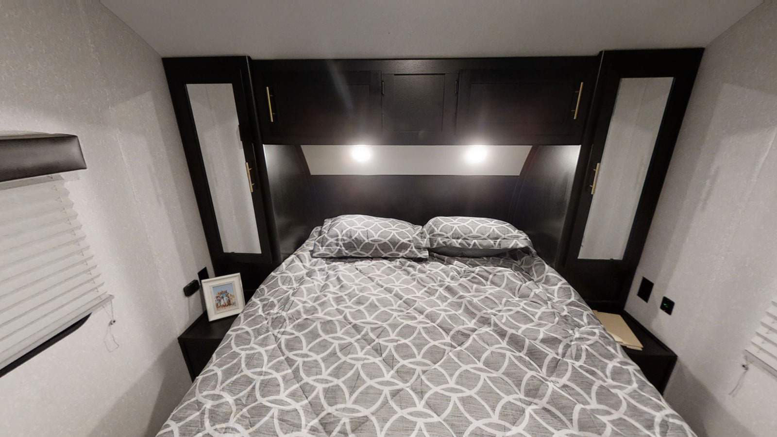 RV rental bedroom: a comfortable space featuring a patterned bed, overhead cabinets, and bedside lights, ready for your trip.. Forest River Cherokee Grey Wolf 2020
