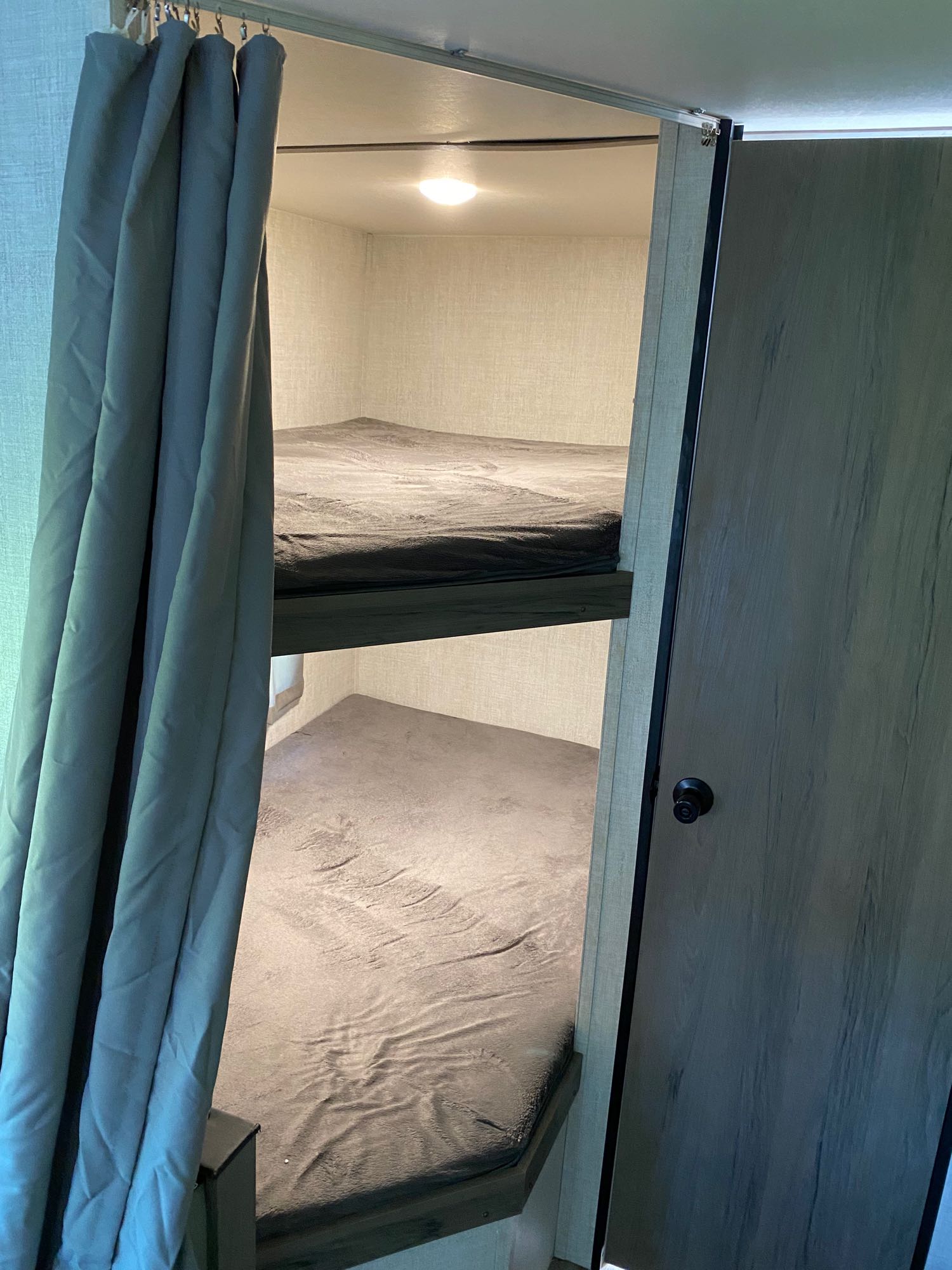 Cozy RV rental sleeping area featuring two bunk beds with grey covers, a privacy curtain, and a nearby door.. Gulf Stream Other 2021