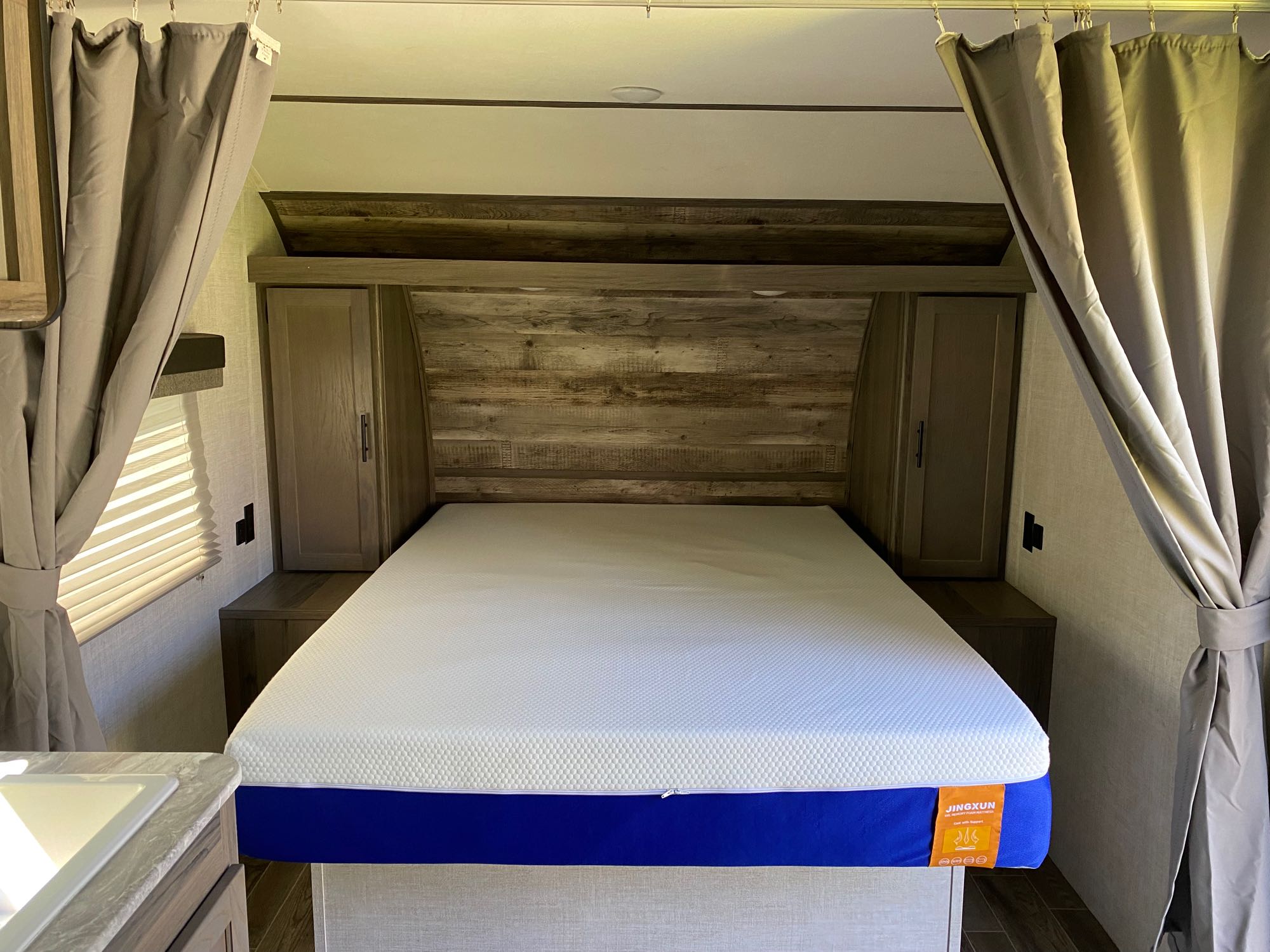 Inside an RV rental: a cozy bedroom features a white and blue mattress, wood headboard, and side cabinets with curtains.. Gulf Stream Other 2021