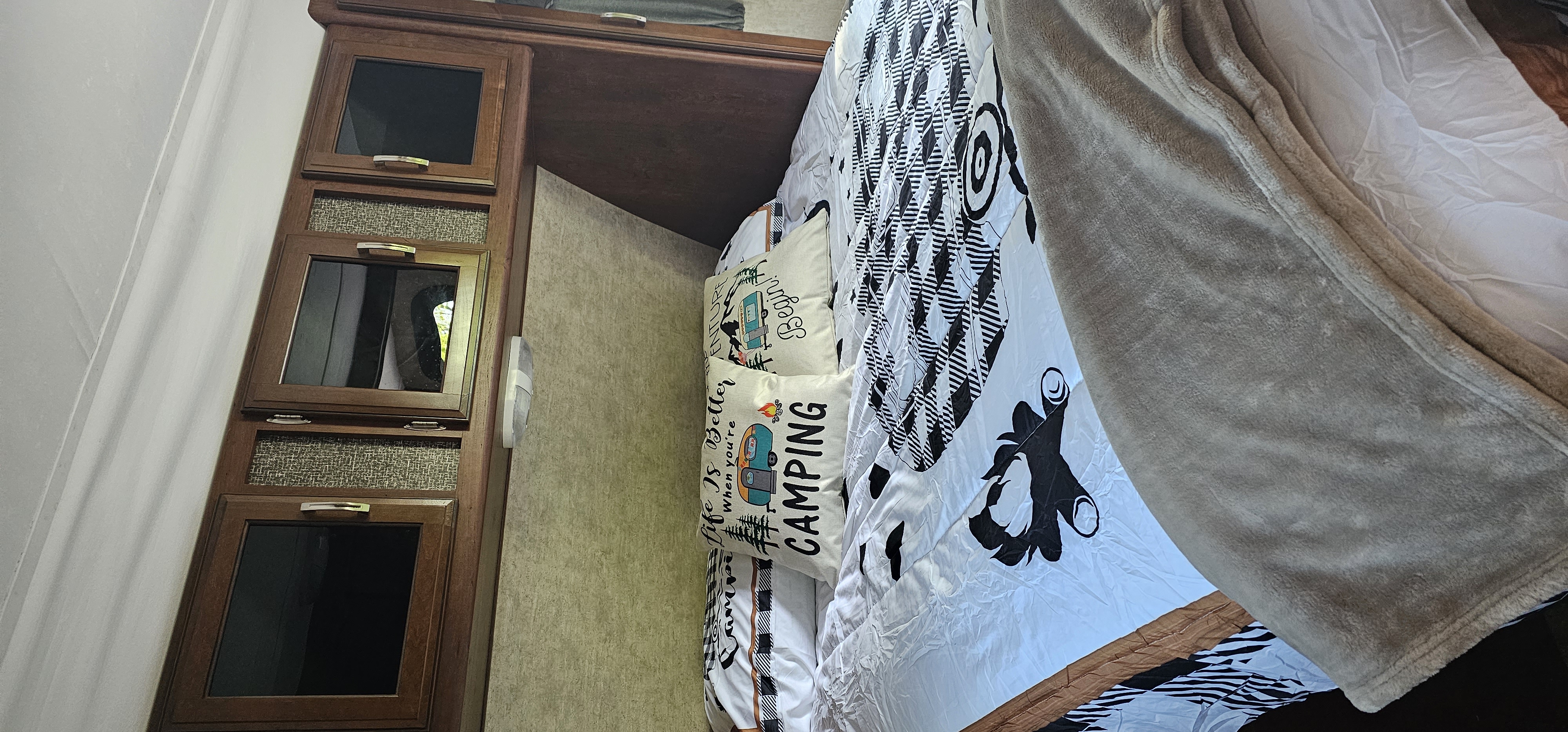 View of an RV rental bedroom featuring a bed with camping-themed pillows and wooden storage.. Keystone RV Passport Grand Touring 2016