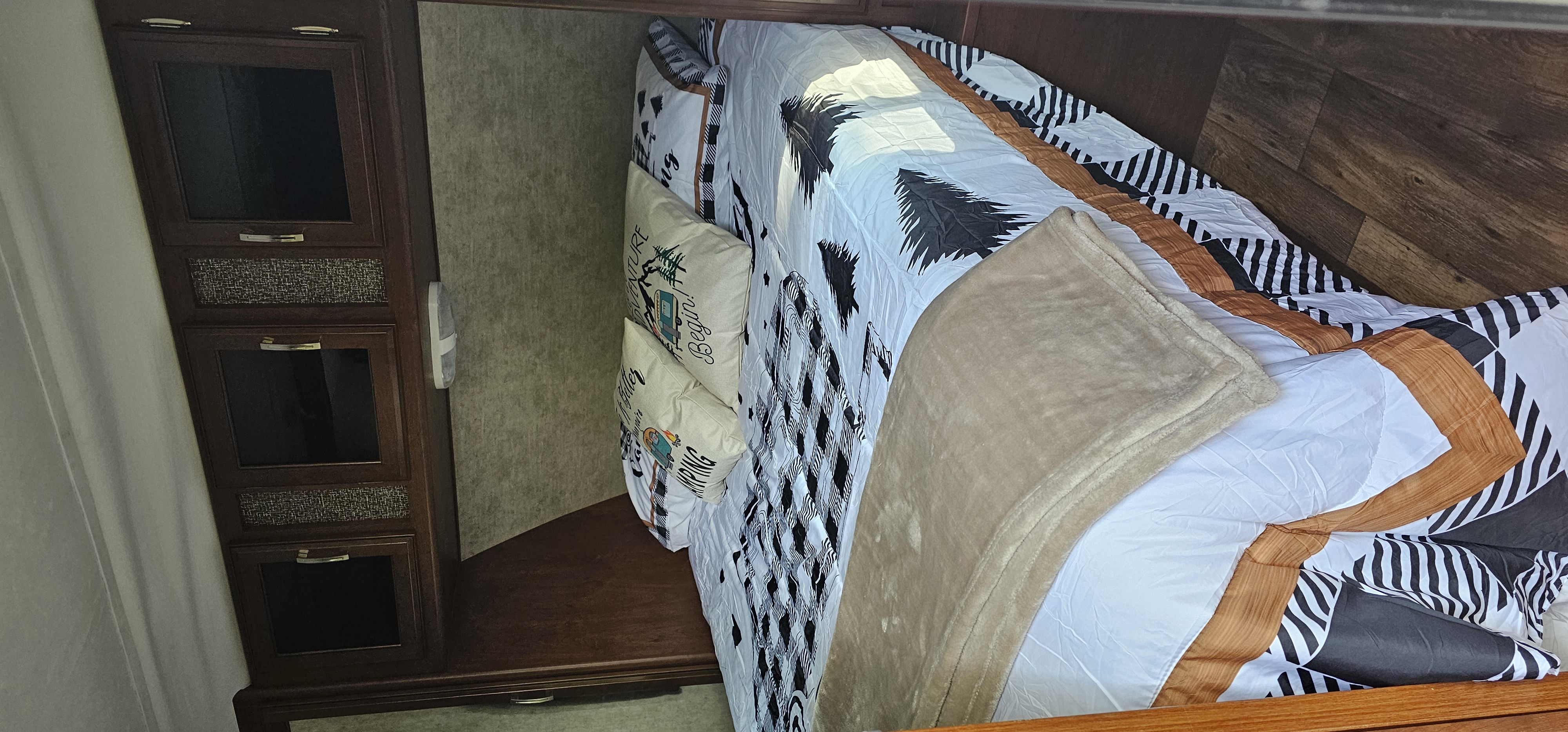 Interior of an RV rental bedroom. Features a bed with patterned bedding, camping pillows, and wooden storage cabinets.. Keystone RV Passport Grand Touring 2016