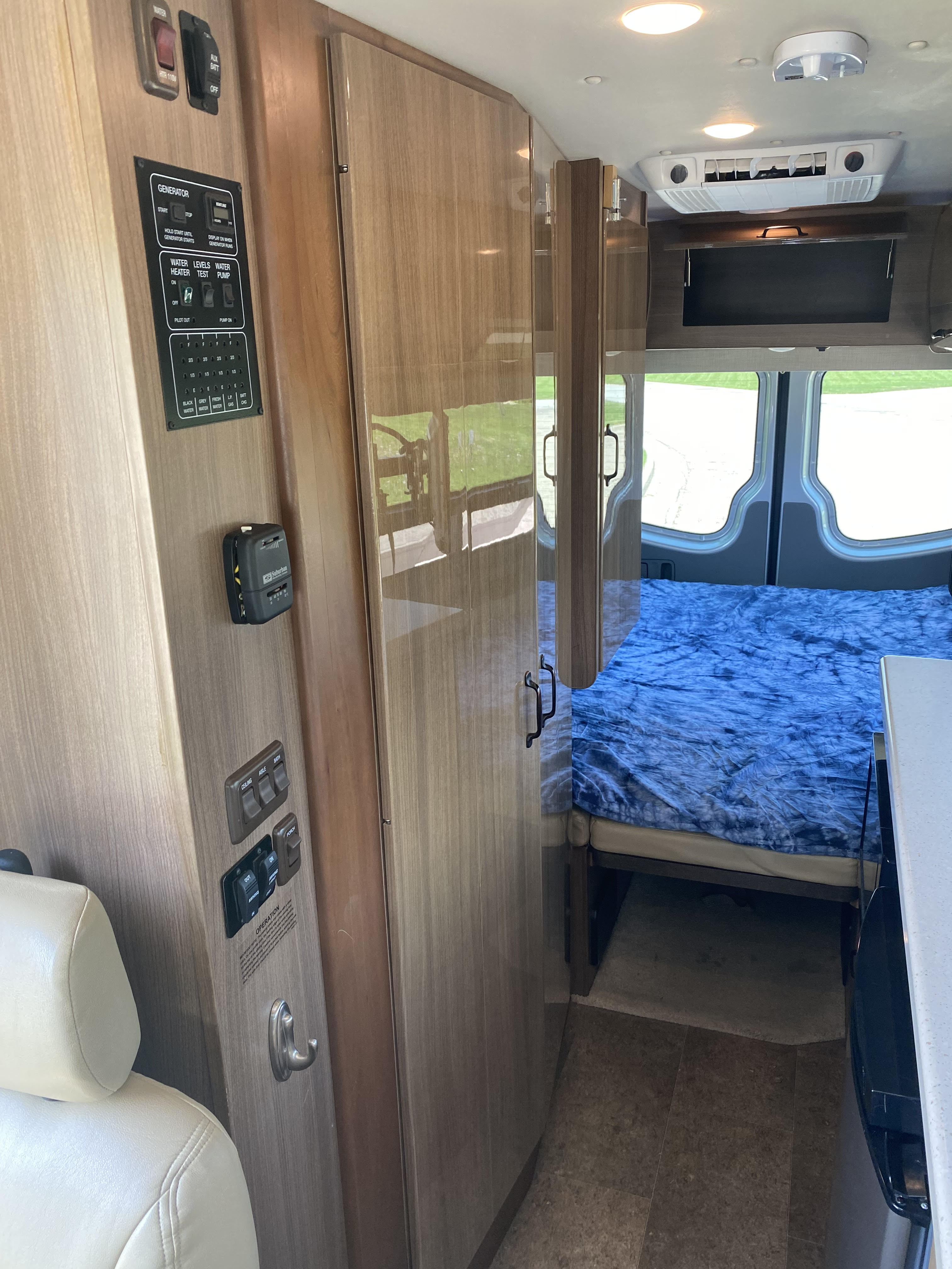 RV rental interior: control panel for generator, water, and lights, with a bed, wood cabinetry, and ceiling-mounted AC.. Winnebago ERA 170X 2014