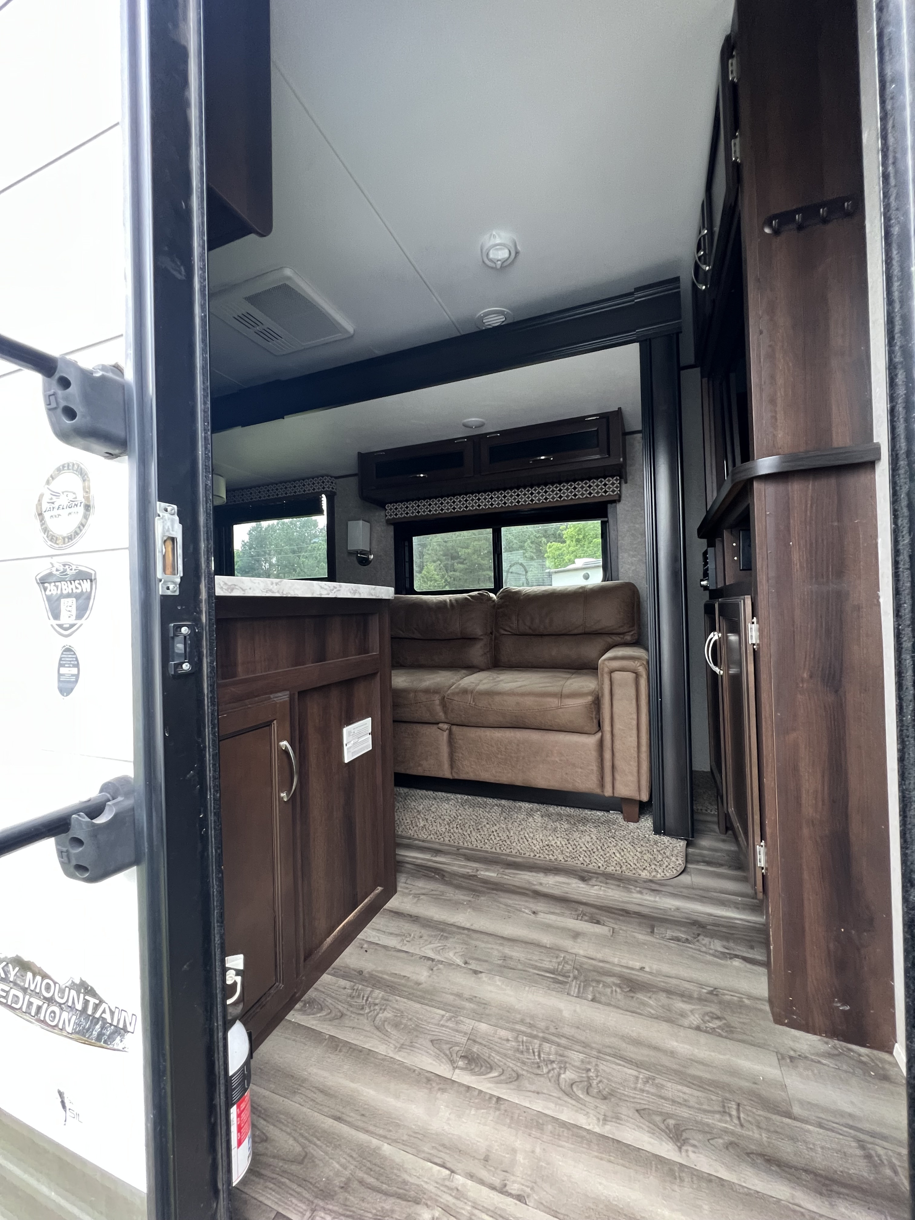 Inside an RV rental: view from the entry showing a brown sofa, kitchen counter, and overhead cabinets in the cozy living space.. Jayco Jay Flight 2018