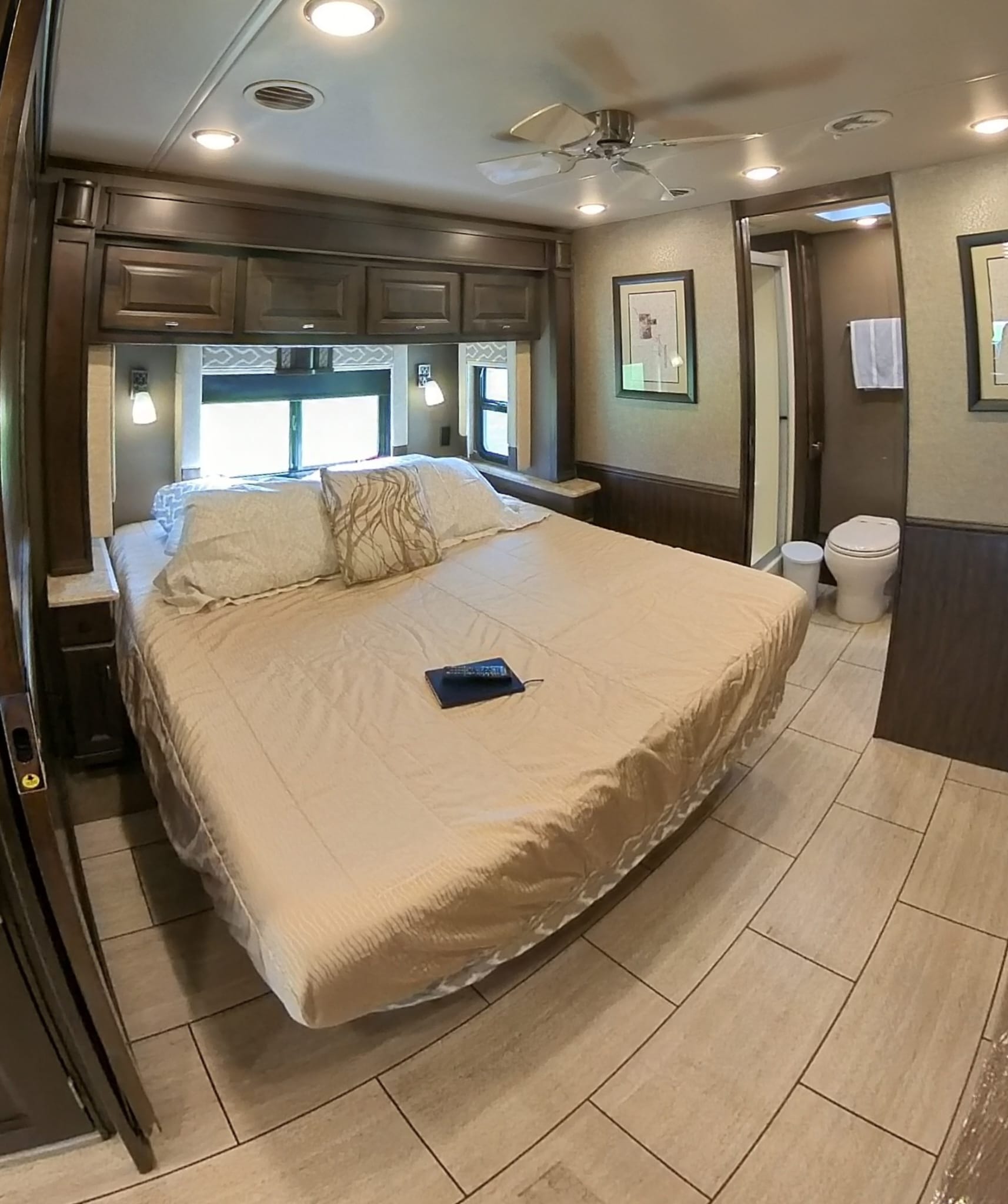 Spacious RV rental bedroom with a comfortable bed, ceiling fan, and tiled floor, leading to an adjacent compact bathroom.. Allegro Allegro Open Road 2018