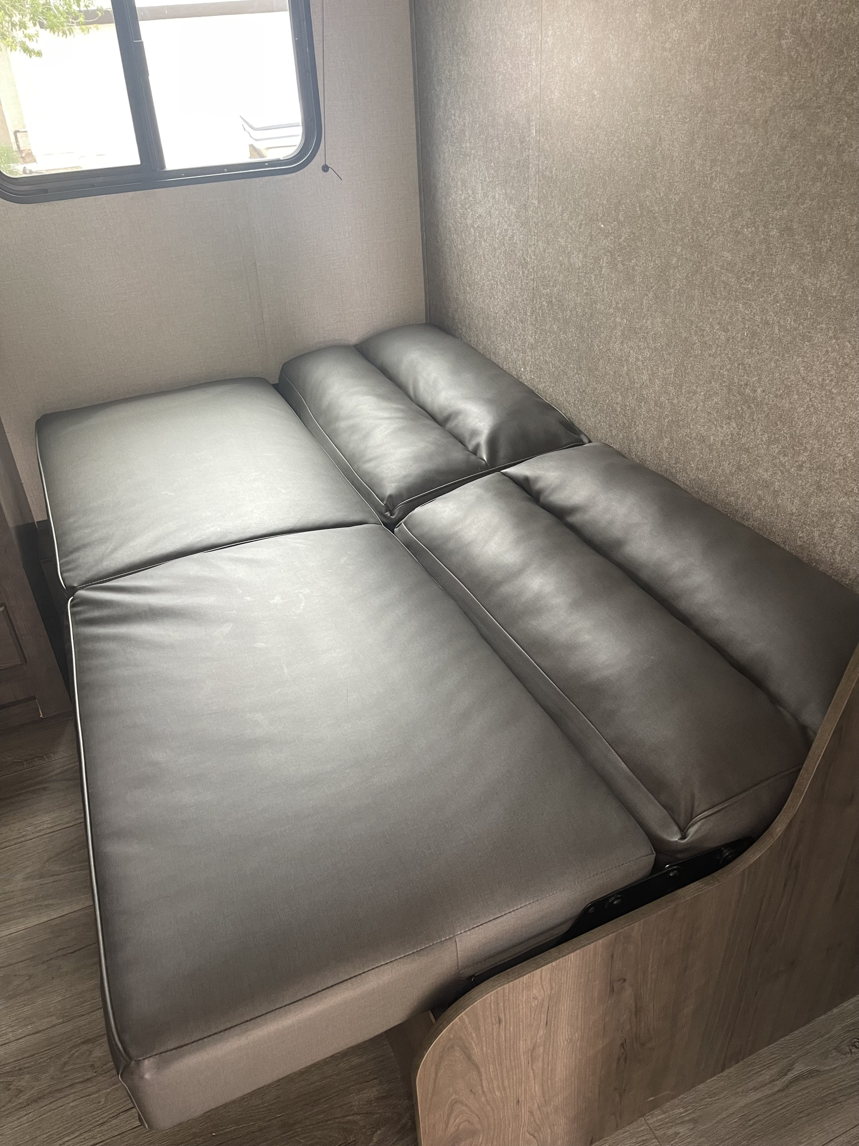 Modern grey convertible sofa/bed in an RV rental. Features sleek upholstery, wood-look trim, and a window. Perfect for an RV interior.. Starcraft Autumn Ridge 2021