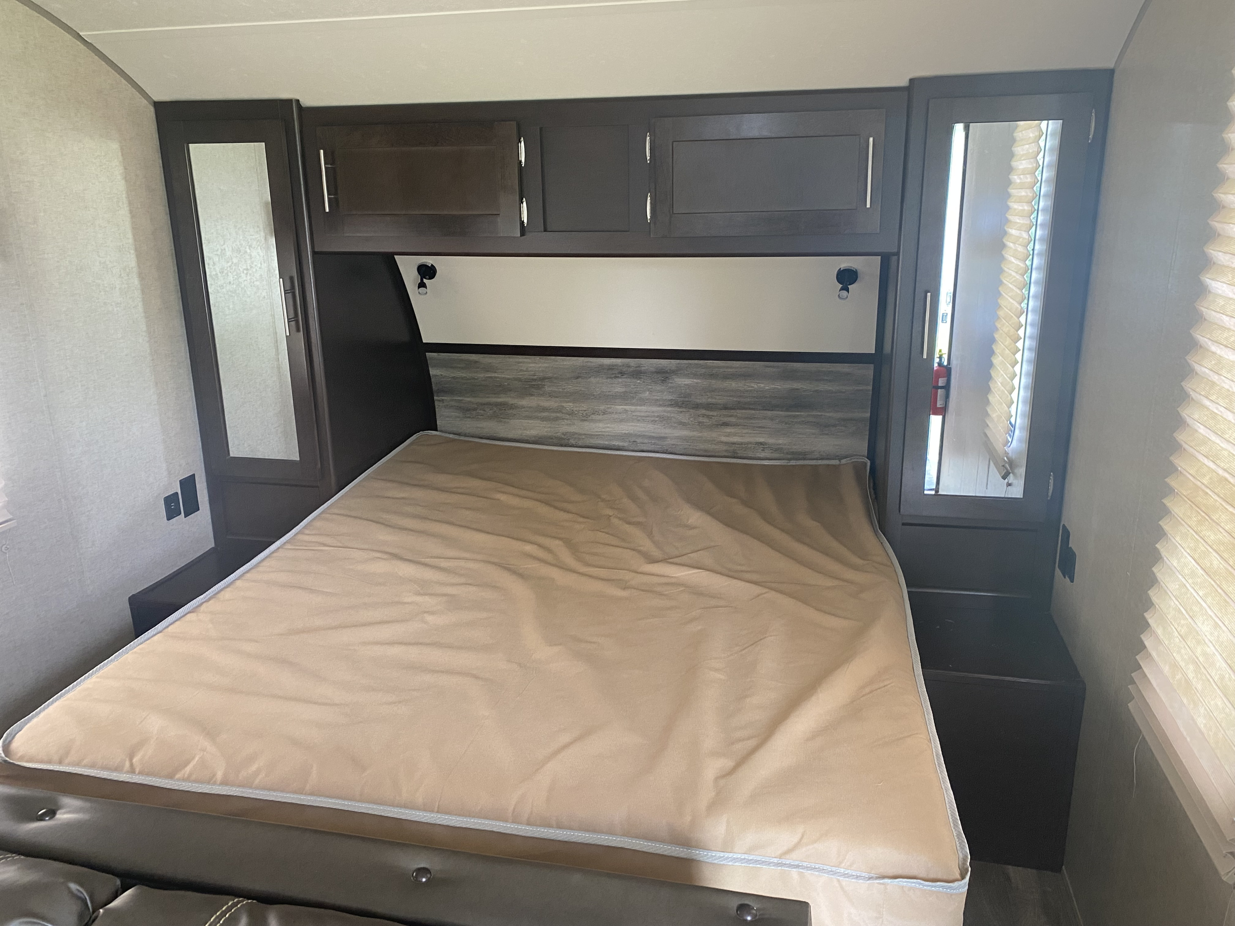 This RV rental bedroom offers a comfortable bed, dark overhead cabinets, side storage with mirrors, and accent lighting.. Forest River Cherokee Grey Wolf 2017
