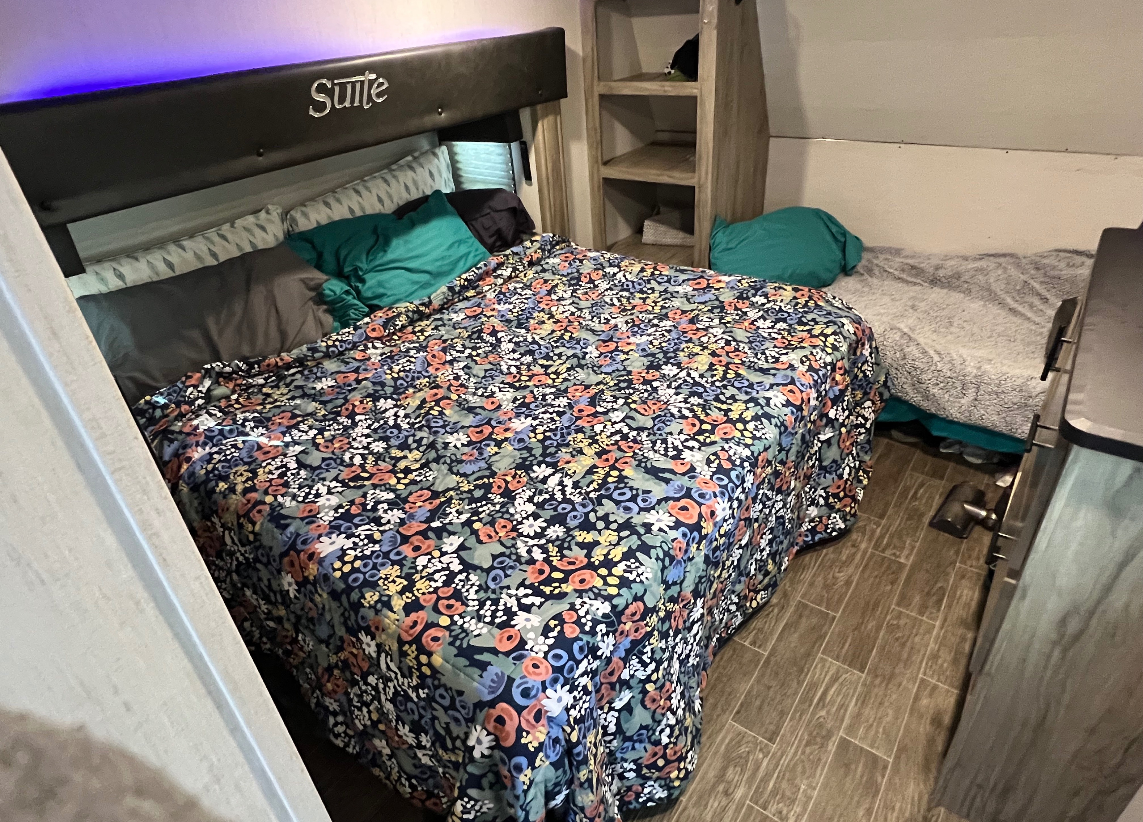 Cozy RV rental bedroom featuring a main bed with floral bedding, purple LED lighting, a bunk bed, and wood-look flooring.. Forest River Wolf Pack 2021